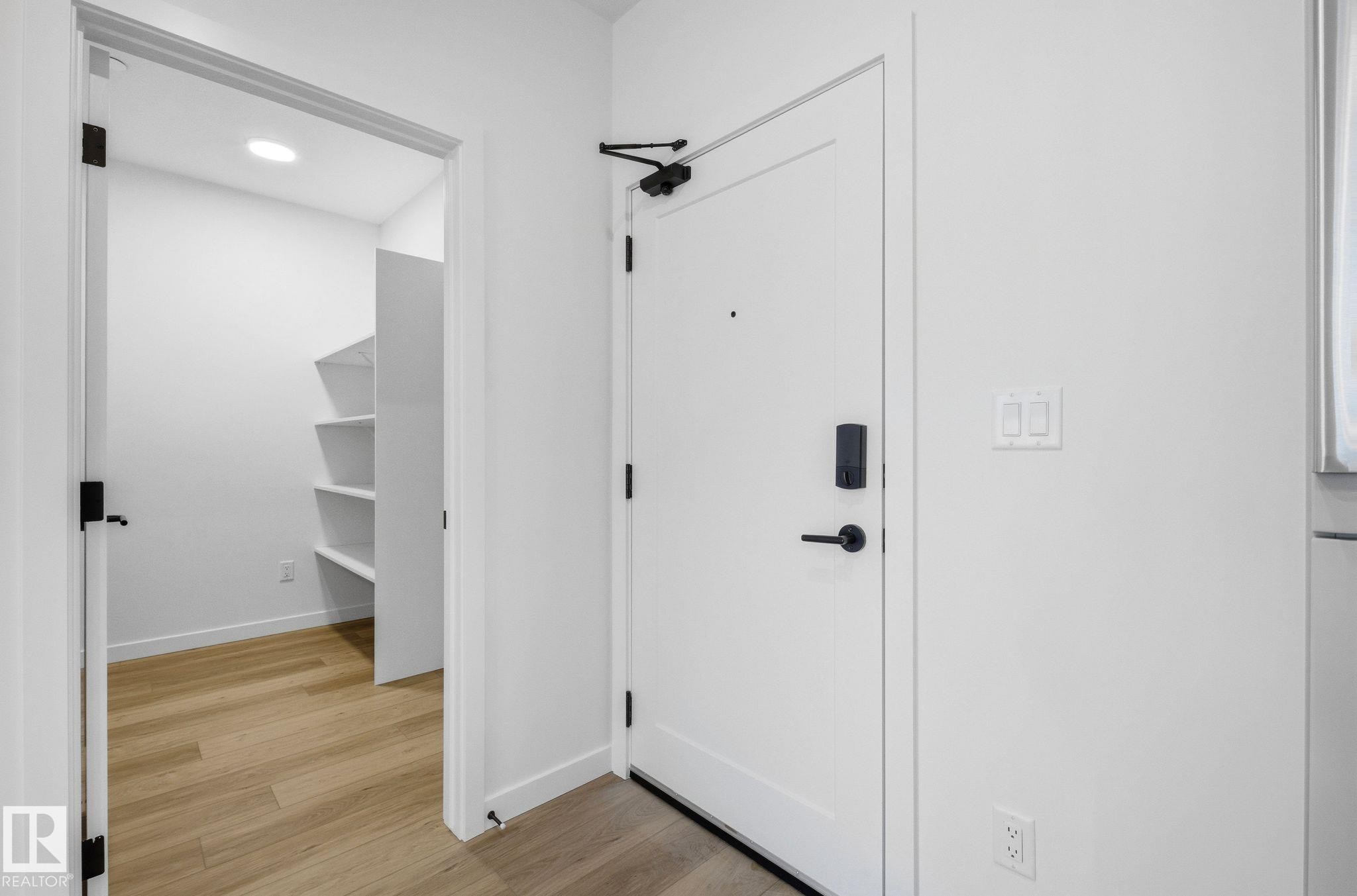 Entryway with a white solid core door featuring matte black hardware and a digital lock - 202 7459 May Common, Edmonton, AB - Indoor Photo Showing Other Room