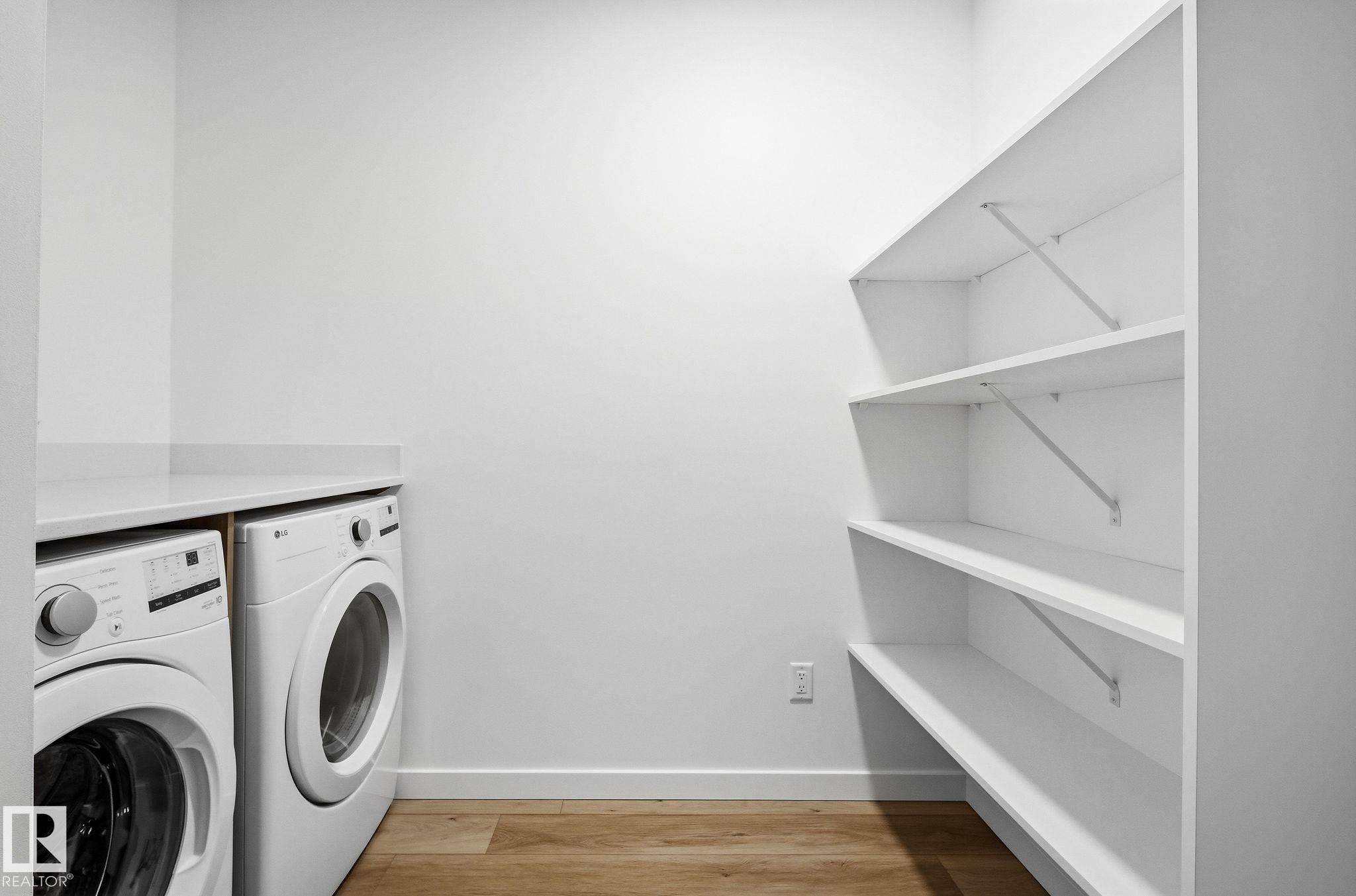 Dedicated laundry area featuring a white countertop, wood-finish flooring, and built-in shelving - 202 7459 May Common, Edmonton, AB - Indoor Photo Showing Laundry Room