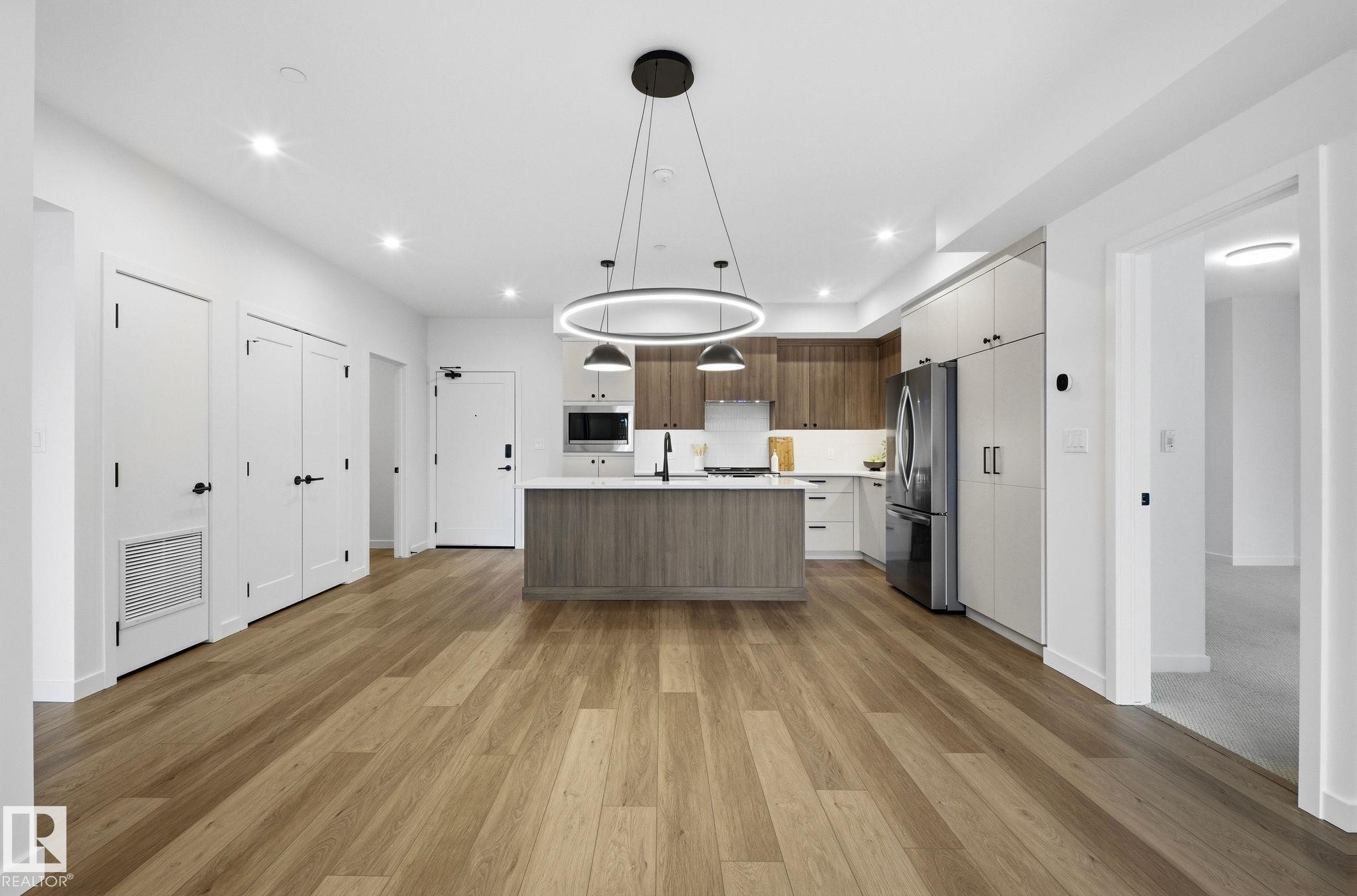 Open-concept living area featuring wood-finish flooring, a kitchen island with seating, pendant lighting, recessed ceiling lights, and contemporary cabinetry - 202 7459 May Common, Edmonton, AB - Indoor Photo Showing Kitchen