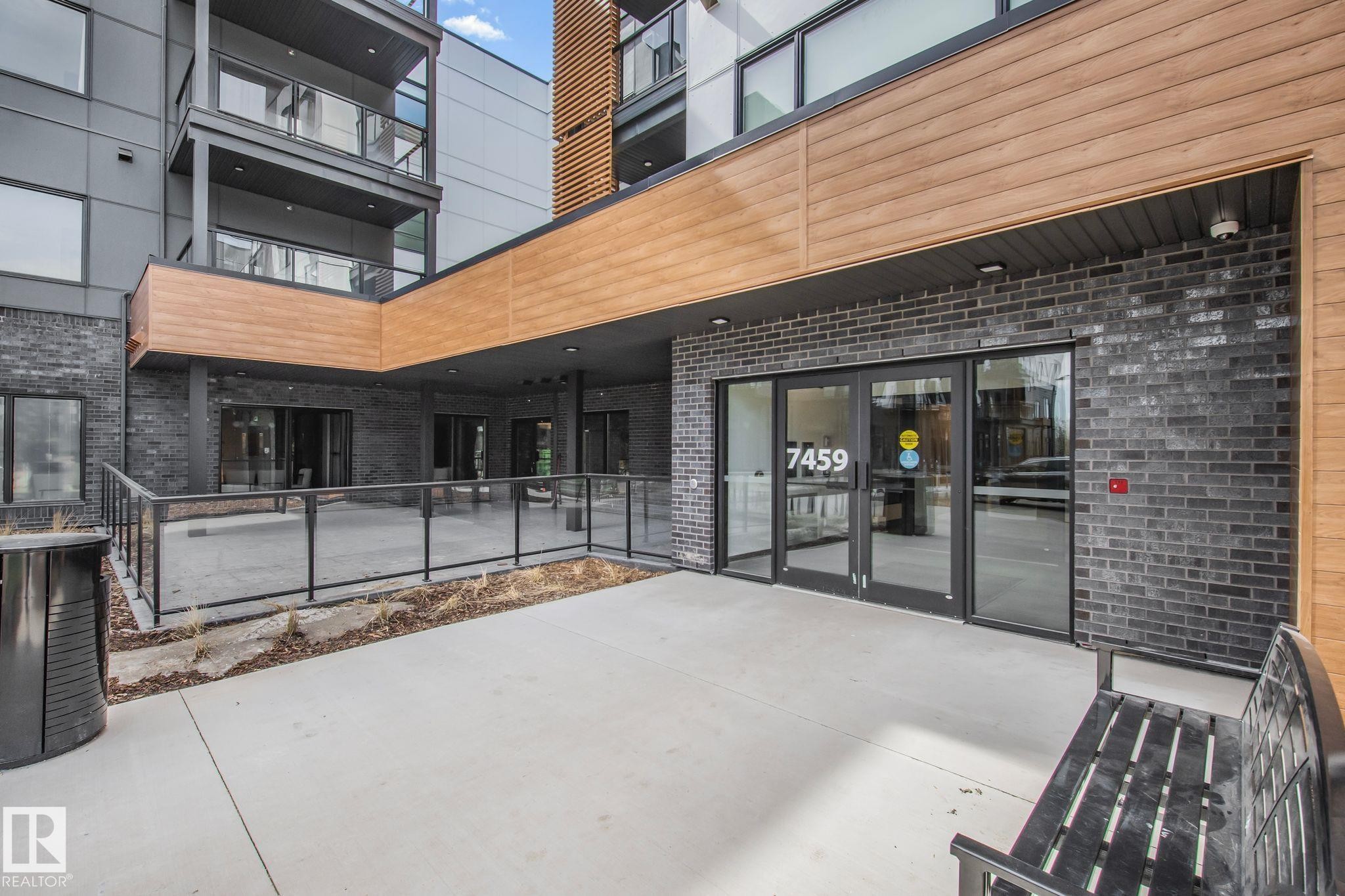 Modern multi-story building entrance featuring dark brick and light wood-finish siding - 202 7459 May Common, Edmonton, AB - Outdoor With Balcony With Exterior