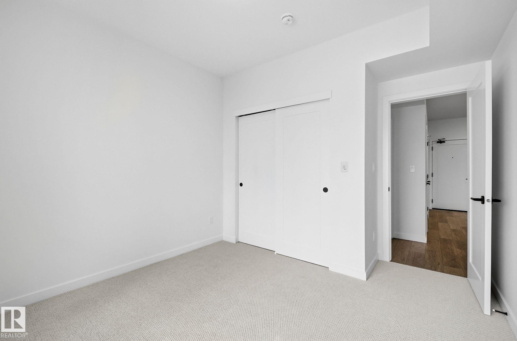 Carpeted room featuring a double-door closet with black hardware - 202 7459 May Common, Edmonton, AB - Indoor Photo Showing Other Room