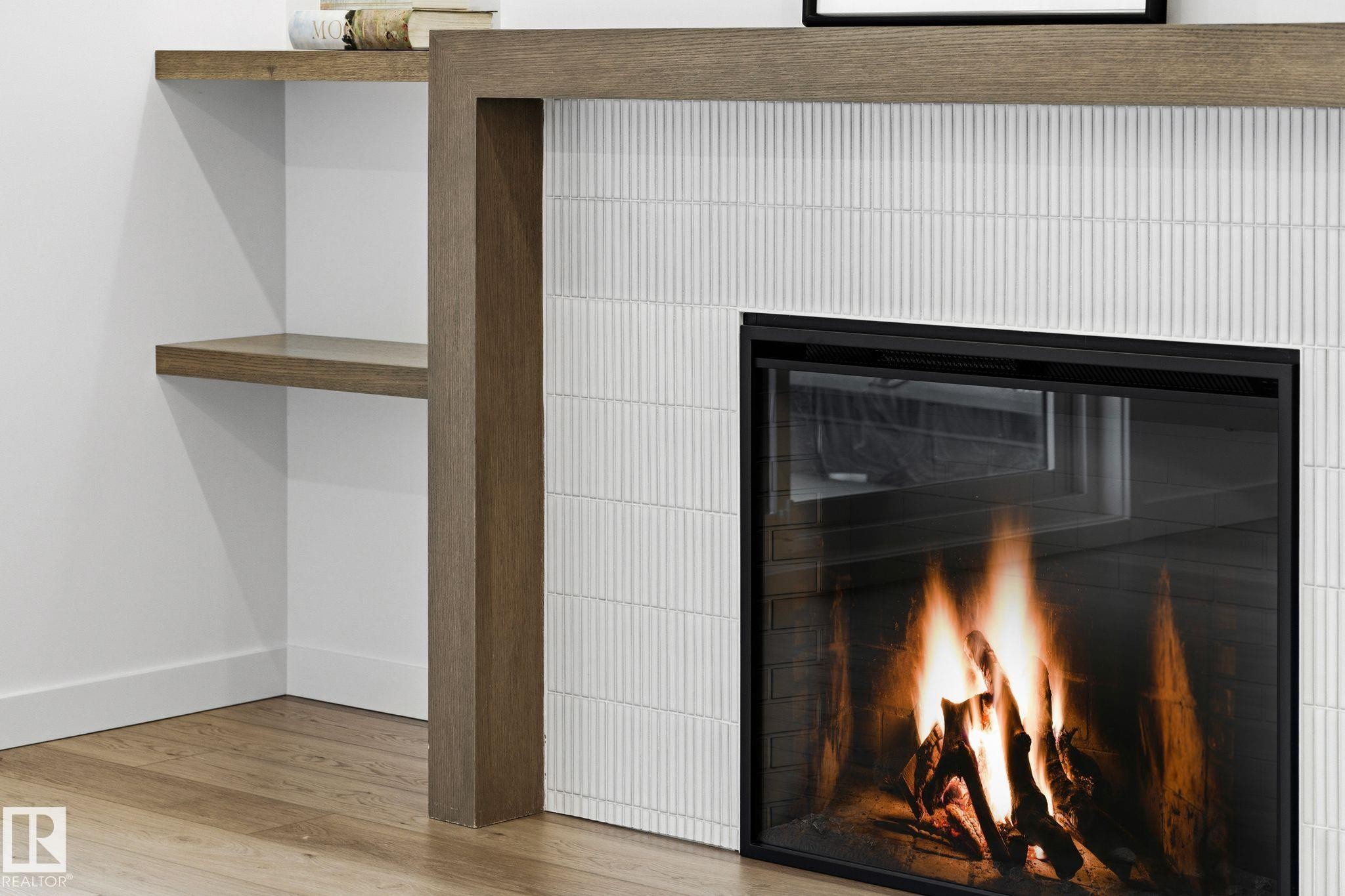 Modern fireplace featuring a textured tile surround, wood-finish mantel, and built-in shelving - 202 7459 May Common, Edmonton, AB - Indoor Photo Showing Other Room With Fireplace