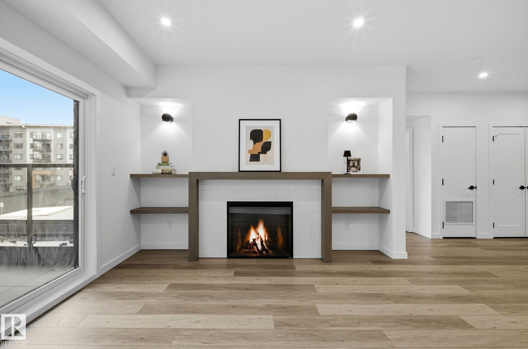 Contemporary electric fireplace with a white tile surround and wood-finish mantel - 202 7459 May Common, Edmonton, AB - Indoor With Fireplace