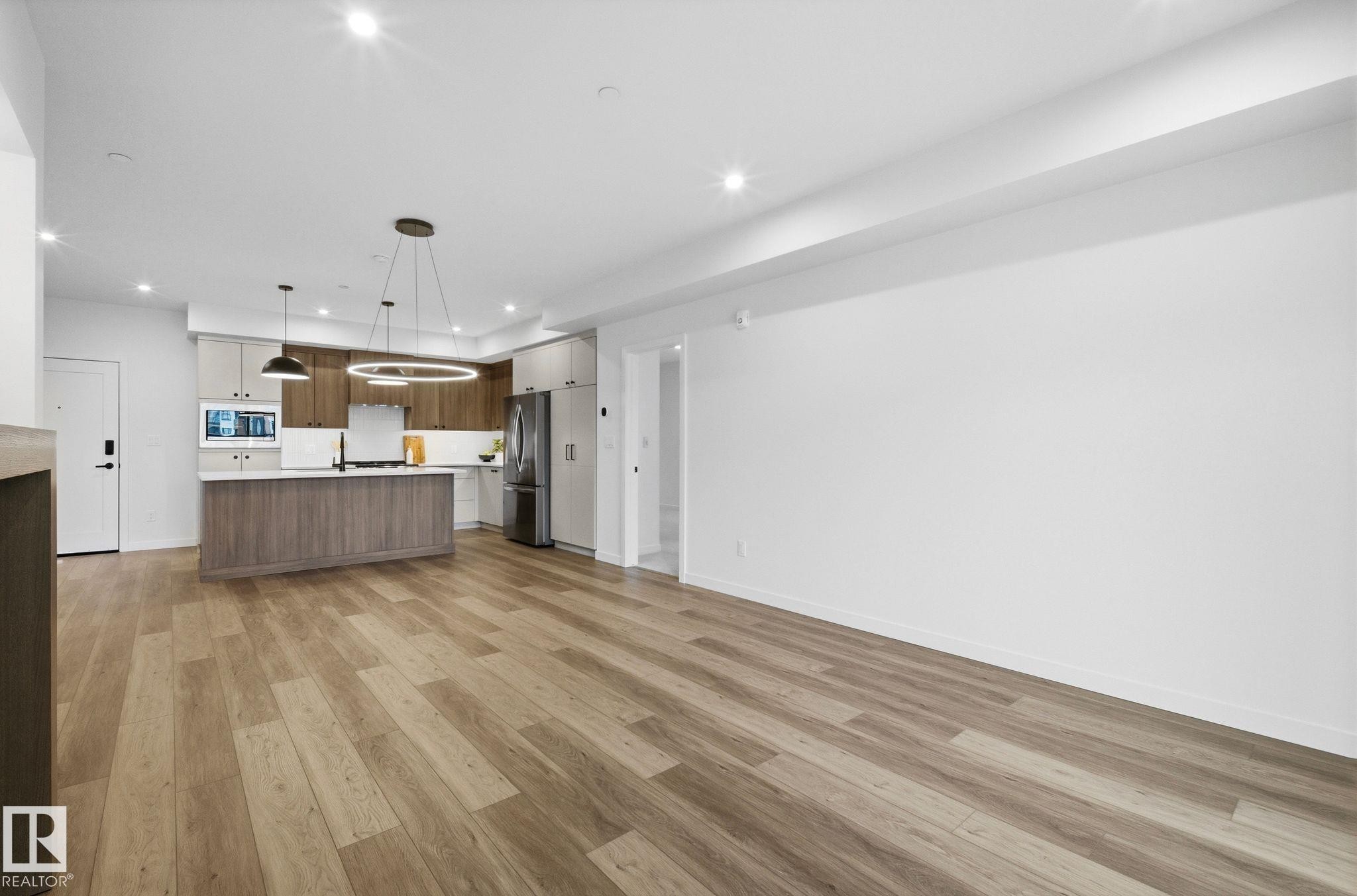 Open-concept living space featuring wood-finish flooring, recessed lighting, and a modern kitchen - 202 7459 May Common, Edmonton, AB - Indoor Photo Showing Kitchen
