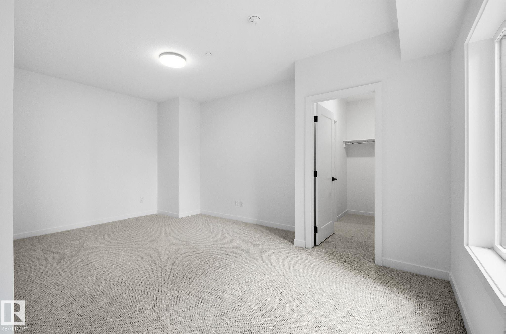 Carpeted room featuring a ceiling-mounted light fixture, white walls, and a window with white trim - 202 7459 May Common, Edmonton, AB - Indoor Photo Showing Other Room
