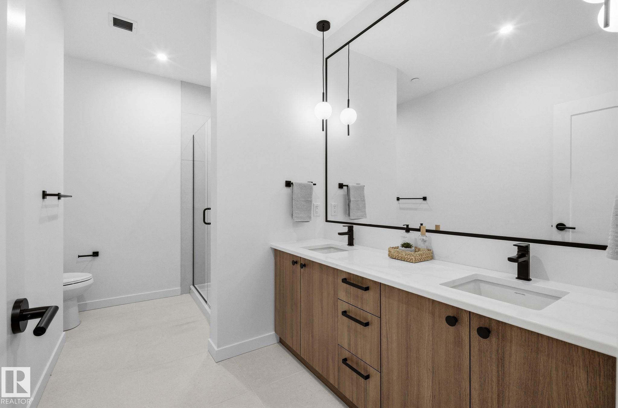 Double vanity with wood-finish cabinetry and white countertops - 202 7459 May Common, Edmonton, AB - Indoor Photo Showing Bathroom
