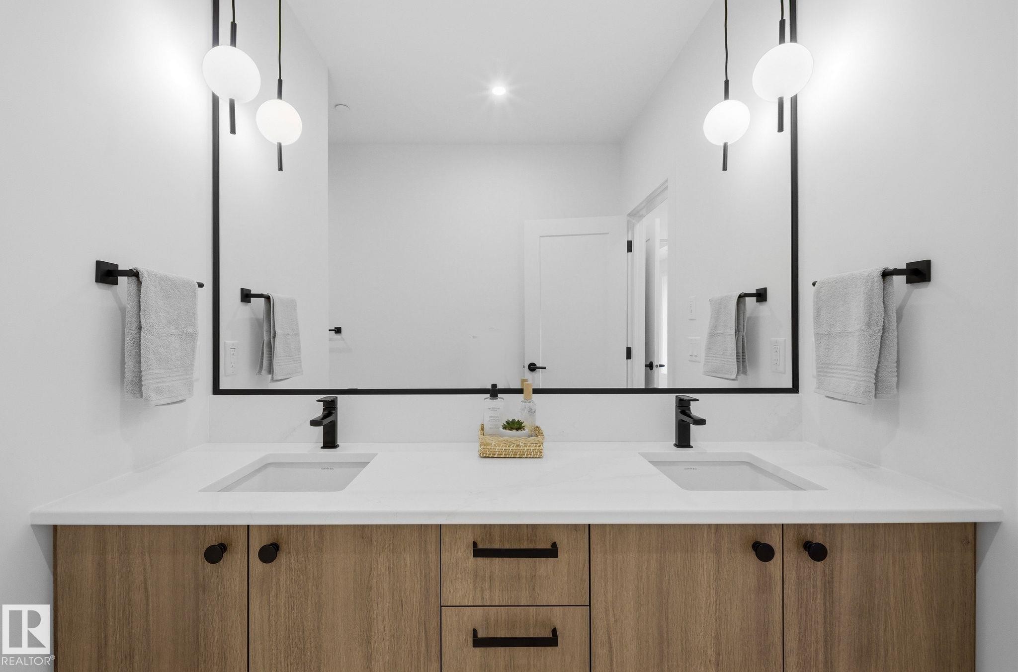 Double vanity with wood-finish cabinetry, integrated sinks, matte black hardware, and a large framed mirror - 202 7459 May Common, Edmonton, AB - Indoor Photo Showing Bathroom