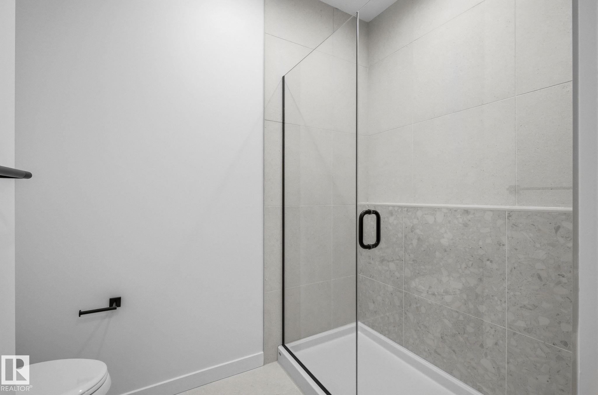 Glass-enclosed shower with matte black hardware, light gray subway tile, and a contrasting light gray stone-finish tile accent - 202 7459 May Common, Edmonton, AB - Indoor Photo Showing Bathroom