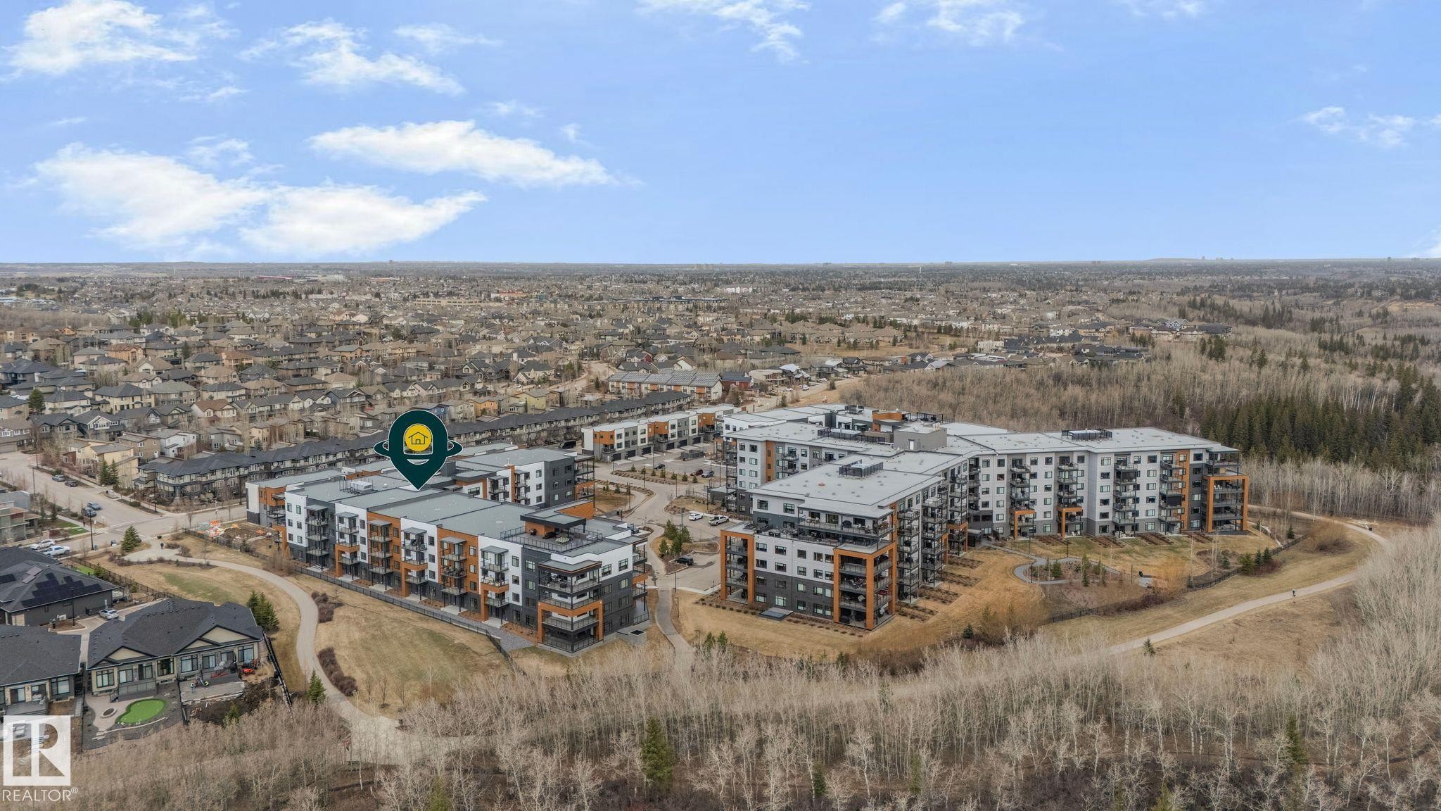Modern multi-story residential buildings featuring balconies and a contemporary facade, surrounded by natural landscaping and suburban development - 202 7459 May Common, Edmonton, AB - Outdoor With View