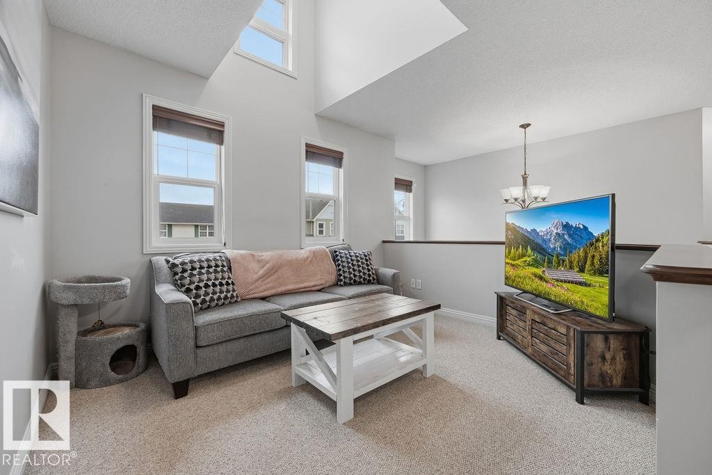 2nd floor bonus room >Loft area featuring high ceilings, upper and lower windows, carpet flooring, a wood-finish media console, and a contemporary chandelier - 1613 Kerr Road, Edmonton, AB - Indoor Photo Showing Living Room