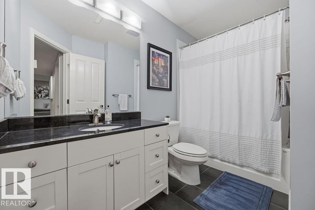 Basement 4 piece Bathroom featuring a white vanity with a dark countertop, an undermount sink, and a mirrored wall - 1613 Kerr Road, Edmonton, AB - Indoor Photo Showing Bathroom
