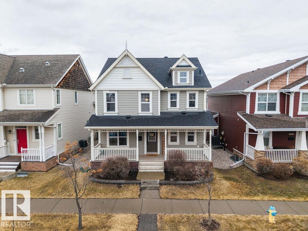 Three-story residence featuring a covered front porch with white railings, a prominent gabled dormer, and a dark shingled roof - 1613 Kerr Road Nw, Edmonton, AB - Outdoor With Facade