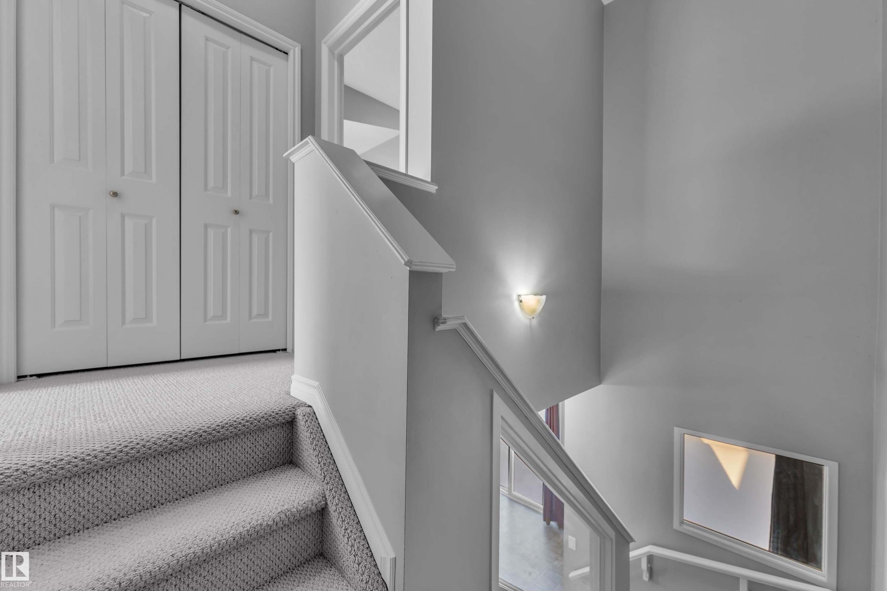 Staircase featuring light gray carpeting, white painted handrails, and a wall-mounted sconce - 110 13825 155, Edmonton, AB - Indoor Photo Showing Other Room