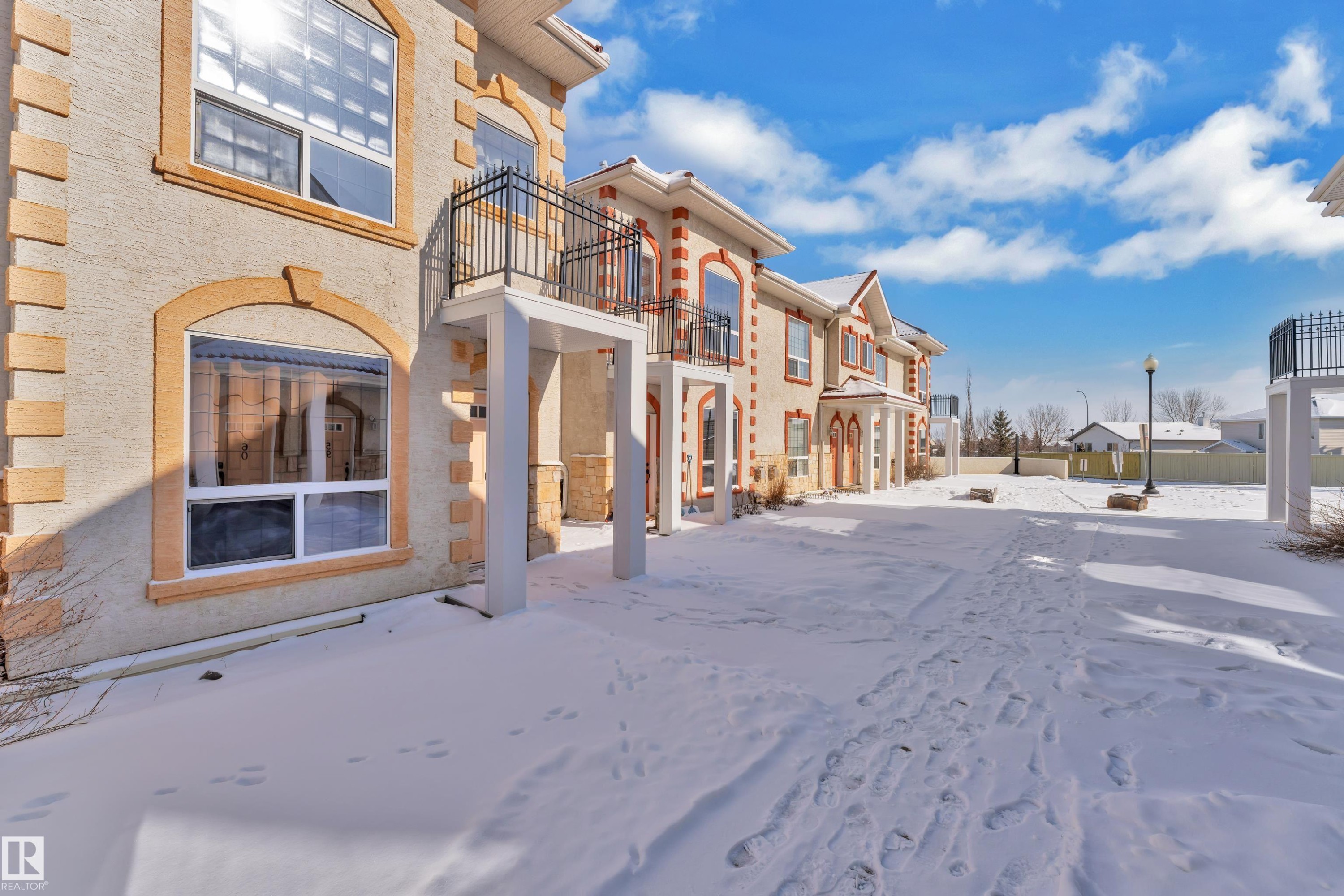 Exterior facade featuring stucco finish with stone accents, arched window frames, and upper-level balconies with wrought iron railings - 110 13825 155, Edmonton, AB - Outdoor