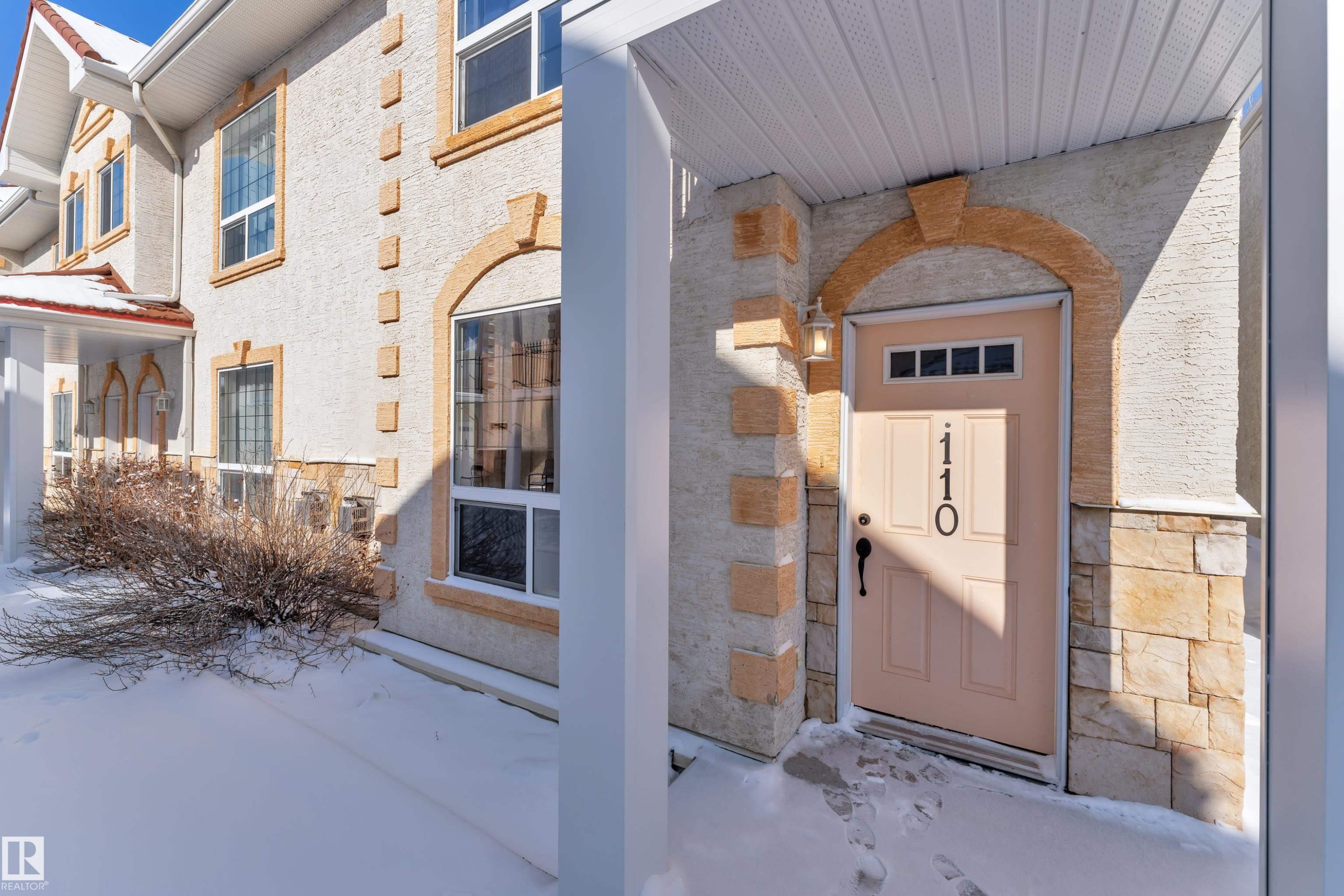 Entryway featuring a panel door with transom windows, accented by a decorative archway and a mounted light fixture - 110 13825 155, Edmonton, AB - Outdoor With Exterior