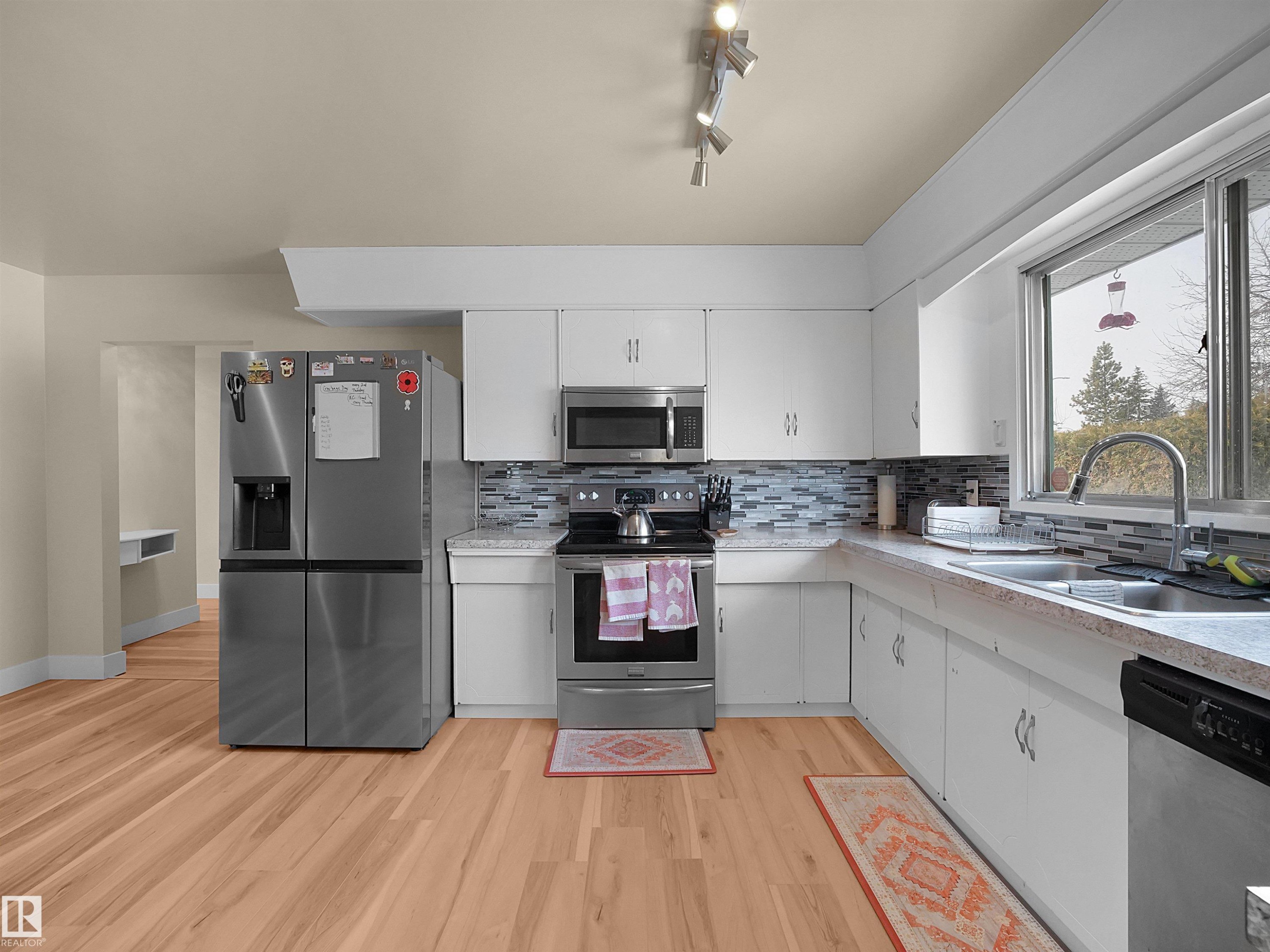 Kitchen featuring wood-finish flooring, white cabinetry, and stainless steel appliances including a refrigerator, range, microwave, and dishwasher - 11044 166 Avenue, Edmonton, AB - Indoor Photo Showing Kitchen With Double Sink