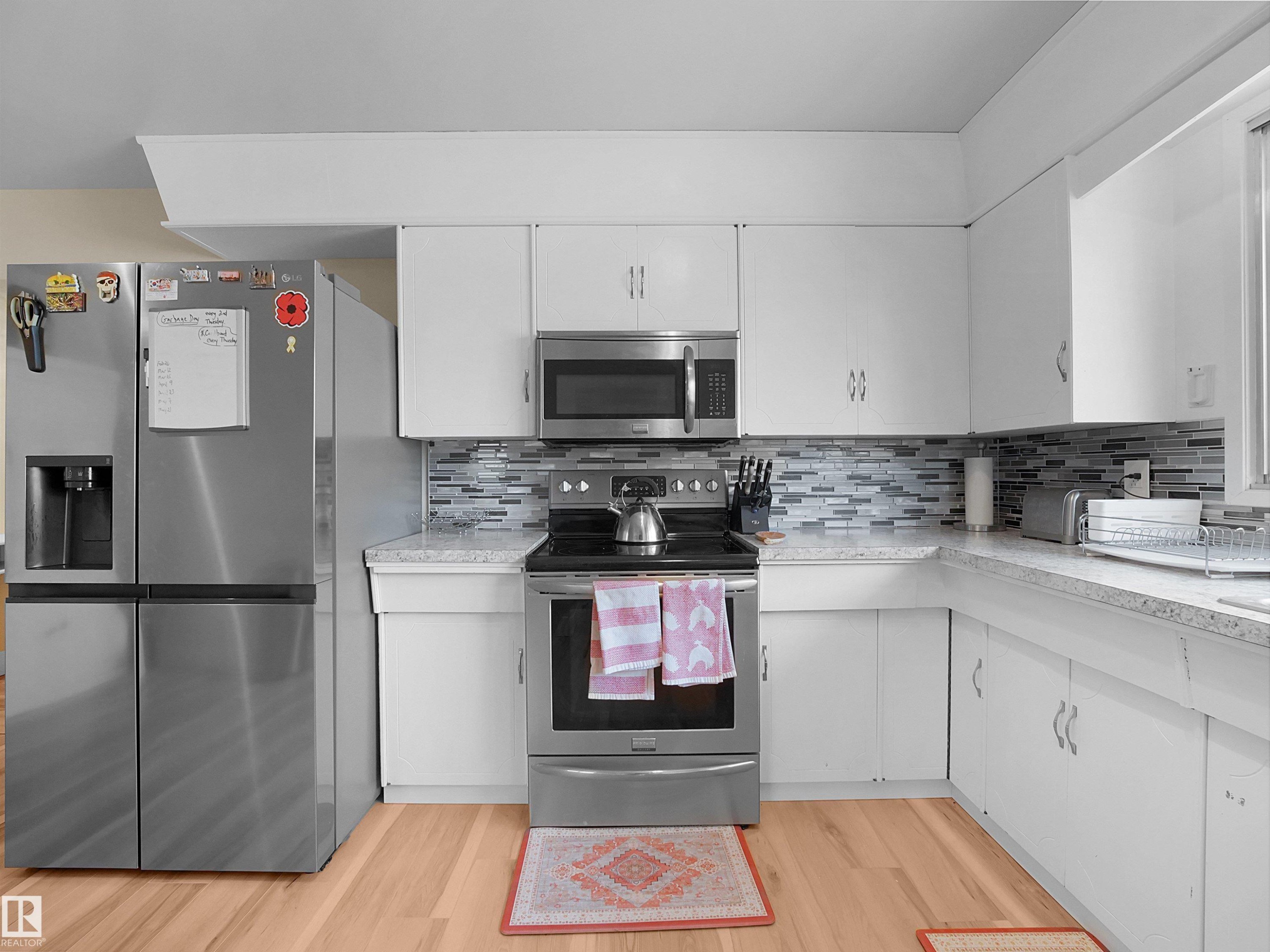 Kitchen featuring stainless steel appliances, white cabinetry, L-shaped countertops, a tile backsplash, and wood-finish flooring - 11044 166 Avenue, Edmonton, AB - Indoor Photo Showing Kitchen With Stainless Steel Kitchen