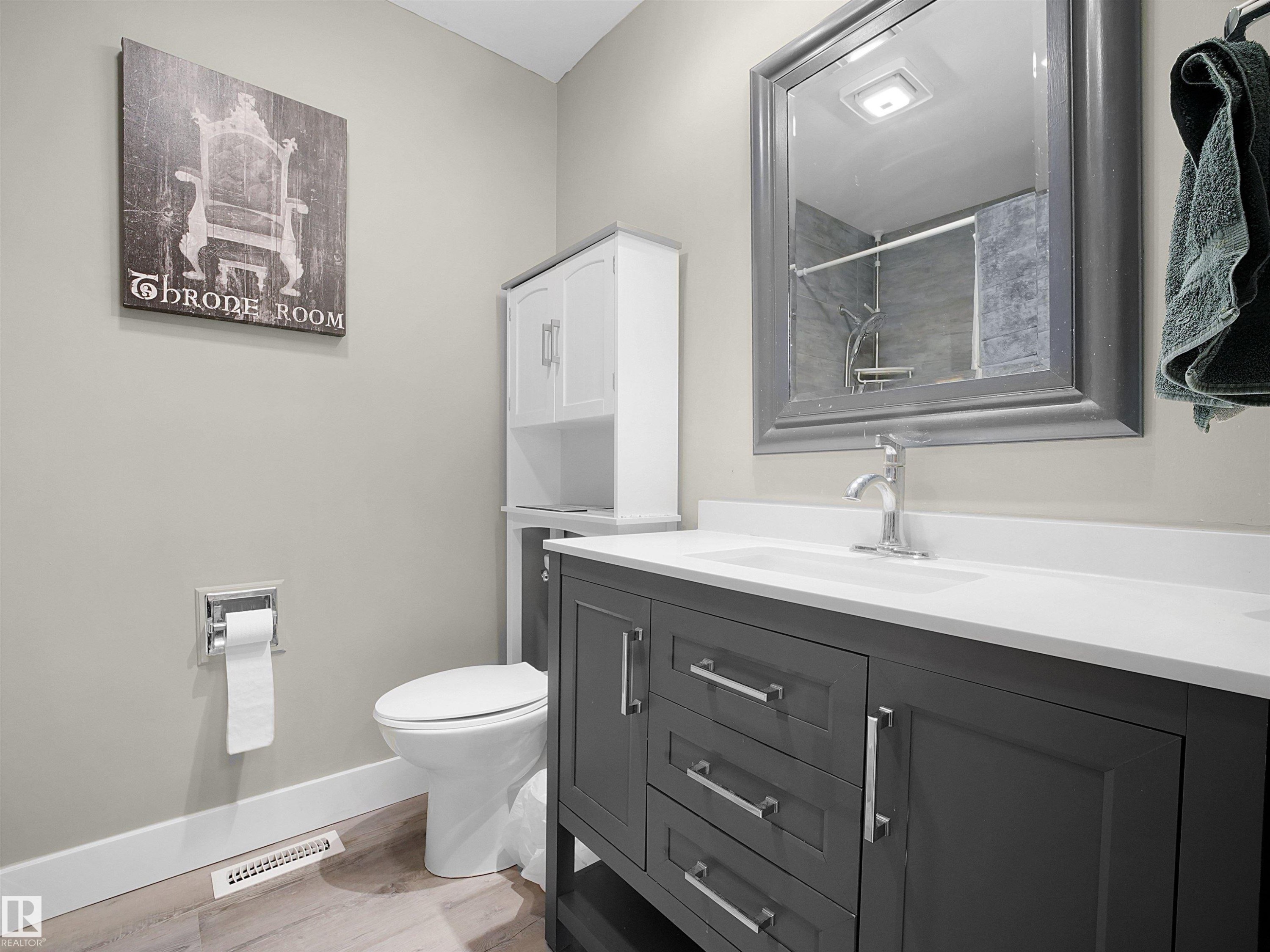 Bathroom featuring a dark gray vanity with chrome hardware, a white countertop with an integrated sink, a framed mirror, and wood-finish flooring - 11044 166 Avenue, Edmonton, AB - Indoor Photo Showing Bathroom