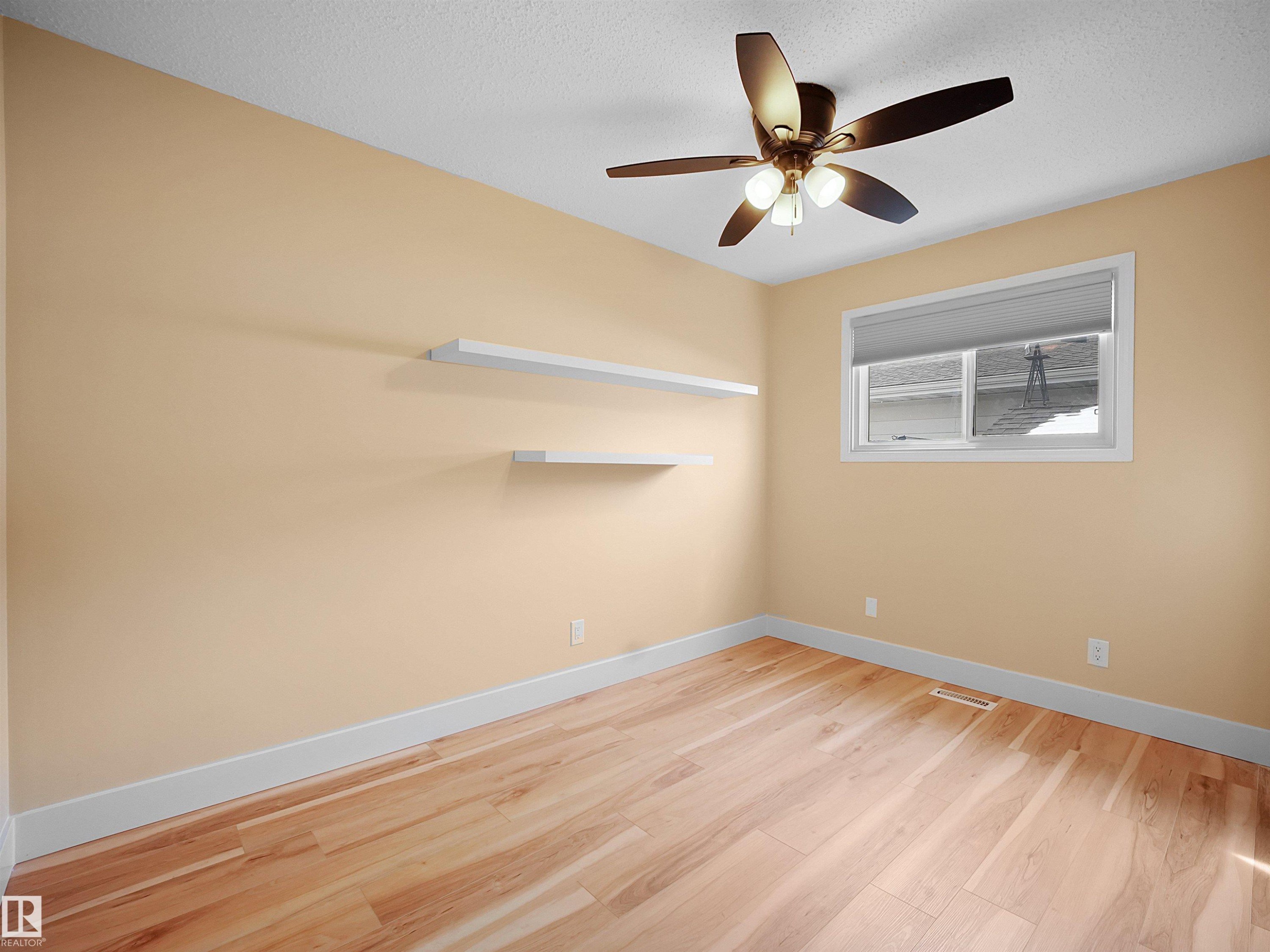 Room featuring wood-finish flooring, a ceiling fan with integrated lighting, a window with a roller shade, and two wall-mounted floating shelves - 11044 166 Avenue, Edmonton, AB - Indoor Photo Showing Other Room