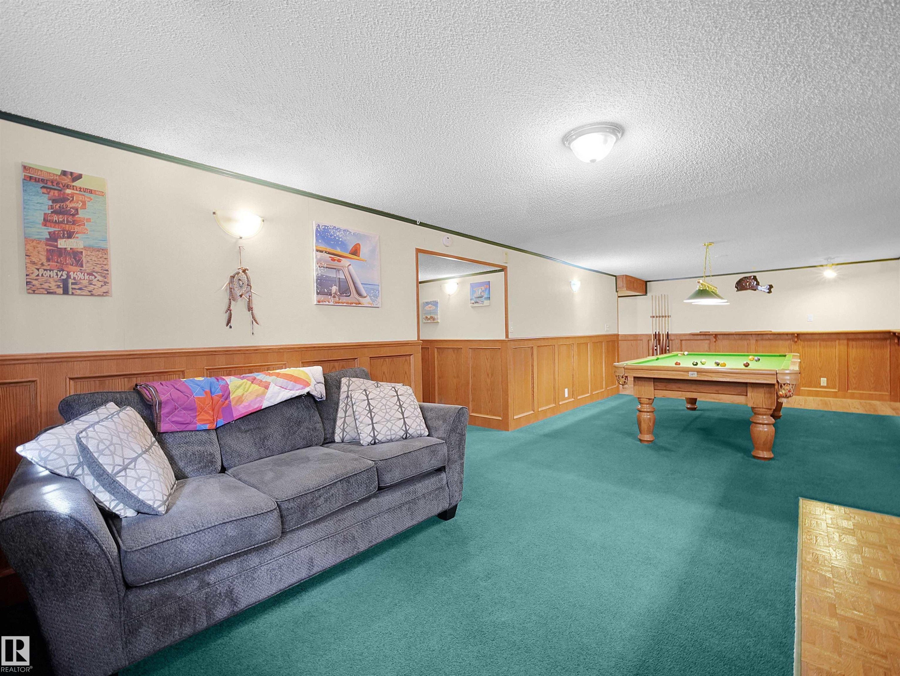Expansive room featuring wall-mounted sconce lighting, wainscoting with wood paneling, and a green-hued carpet flooring - 11044 166 Avenue, Edmonton, AB - Indoor