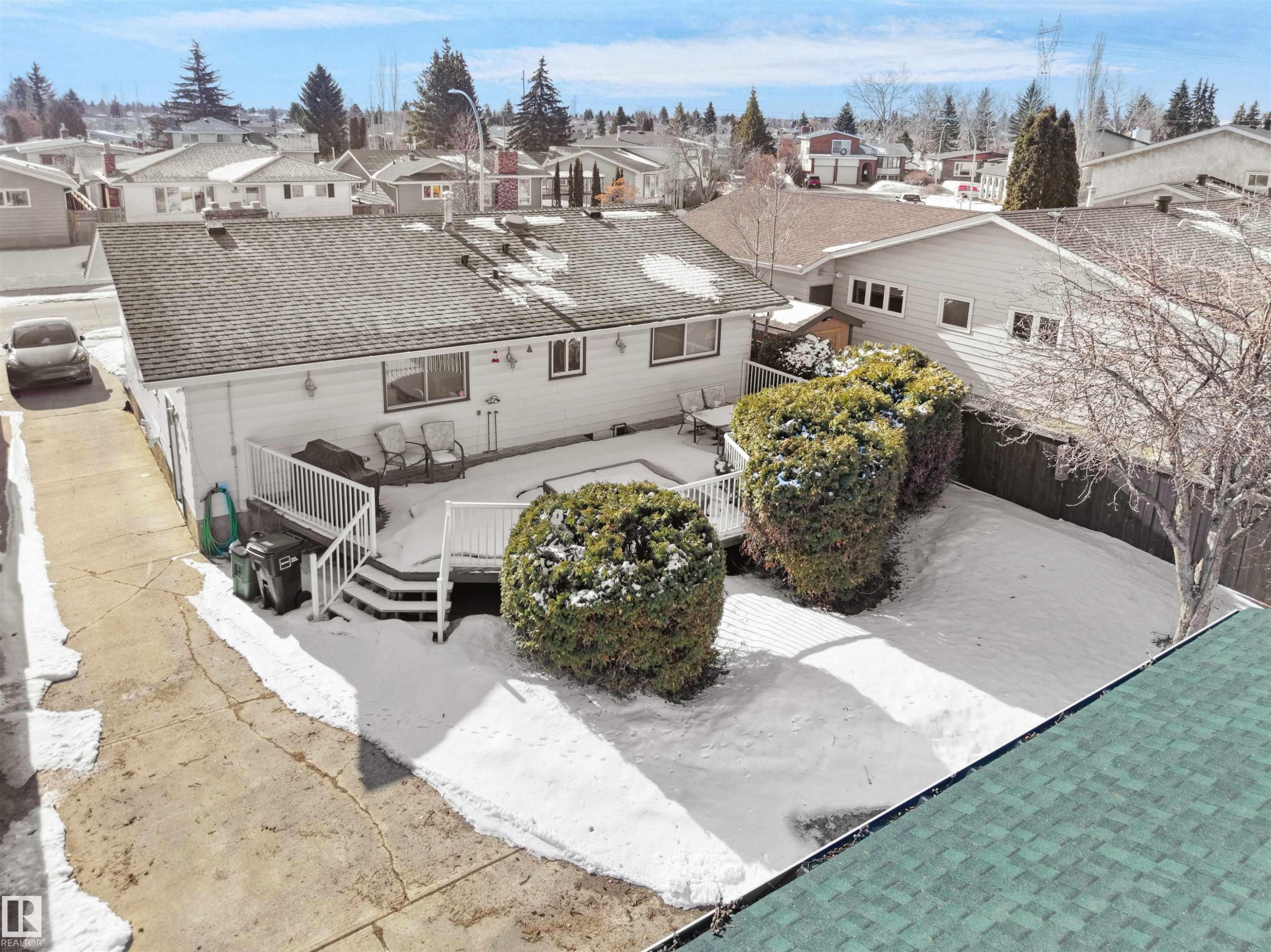 Rear exterior featuring a spacious deck with white railings and stairs, a large backyard area, and established shrubbery - 11044 166 Avenue, Edmonton, AB - Outdoor