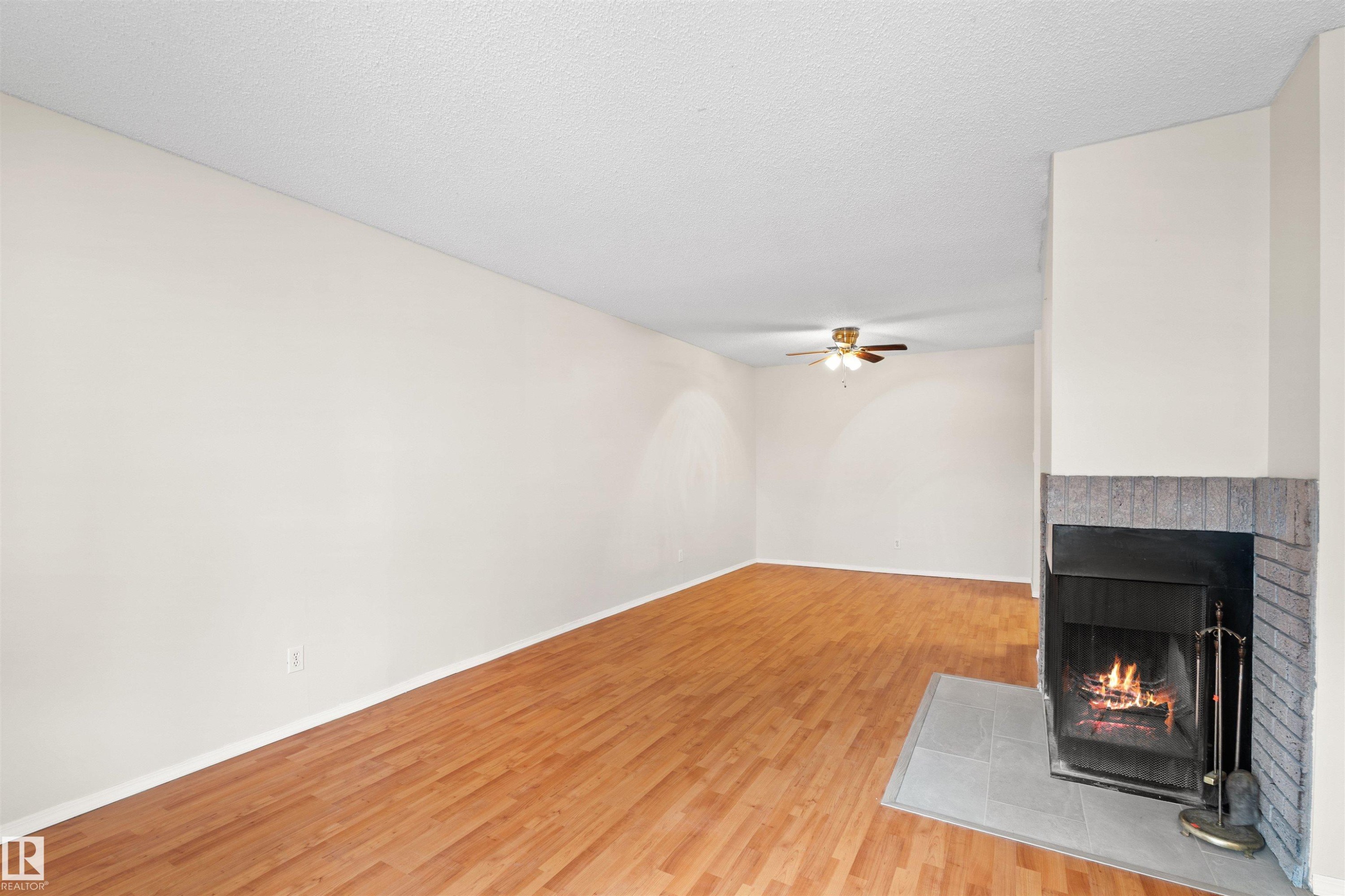 Living area featuring a fireplace with brick and tile surround, wood-finish flooring, and a ceiling fan - 1116 Saddleback Road, Edmonton, AB - Indoor Photo Showing Other Room With Fireplace