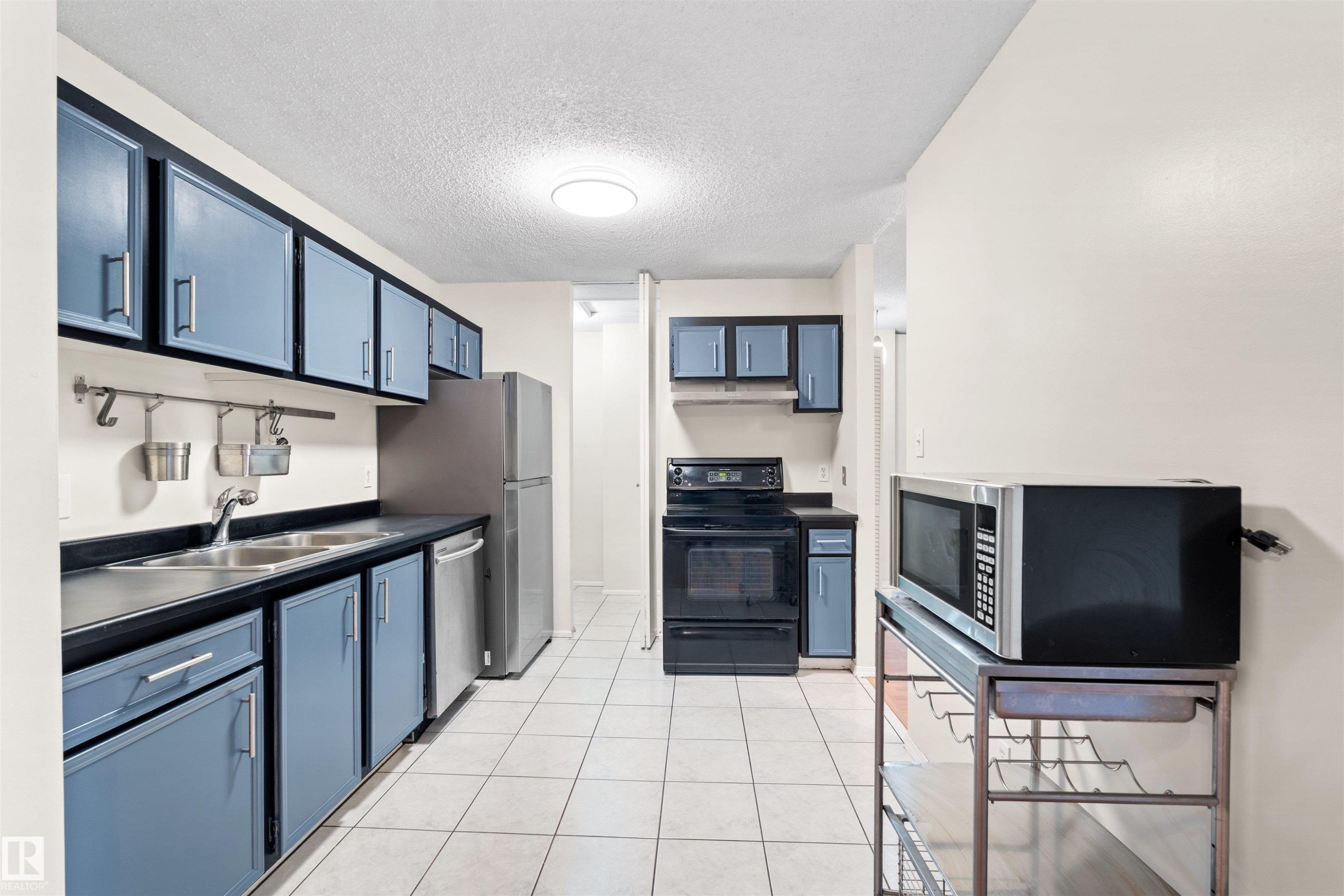 Kitchen featuring blue cabinetry with dark trim, stainless steel appliances, a double basin sink, and white tile flooring - 1116 Saddleback Road, Edmonton, AB - Indoor Photo Showing Kitchen With Double Sink