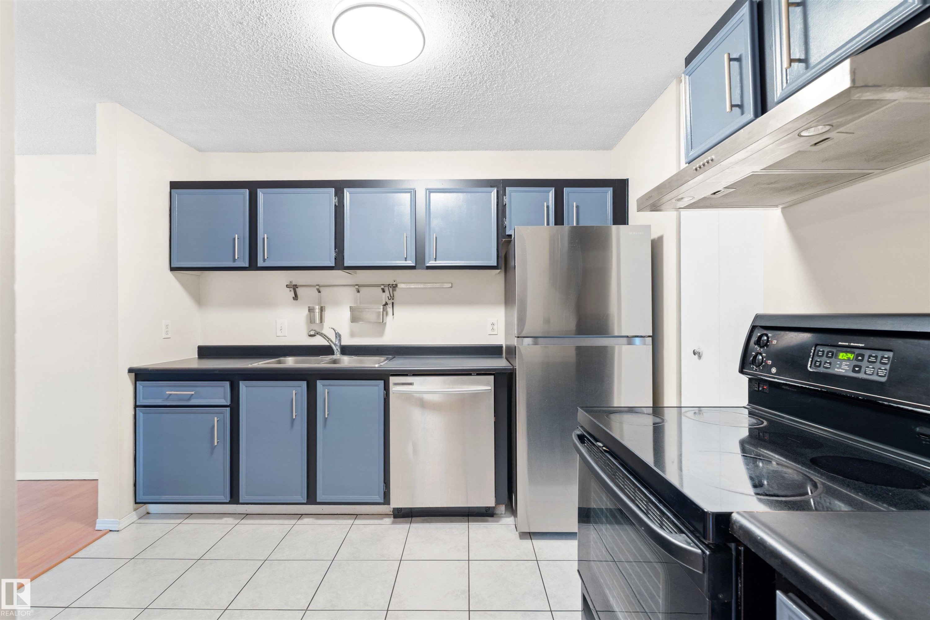 Kitchen featuring blue cabinetry with black framing, stainless steel appliances, dark countertops, and light-toned tile flooring - 1116 Saddleback Road, Edmonton, AB - Indoor Photo Showing Kitchen With Double Sink