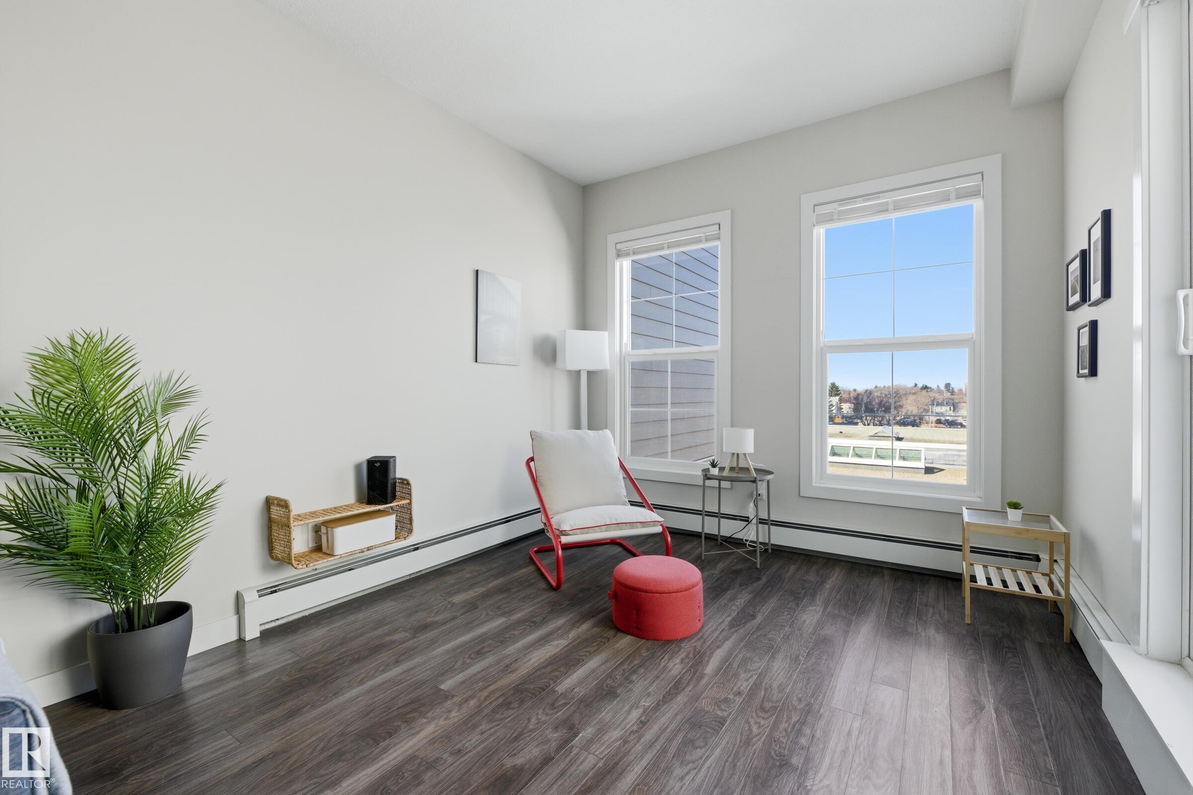 Bright room featuring two large windows, wood-finish flooring, white baseboards, and a built-in wall shelf - 403 10418 81 Avenue, Edmonton, AB - Indoor