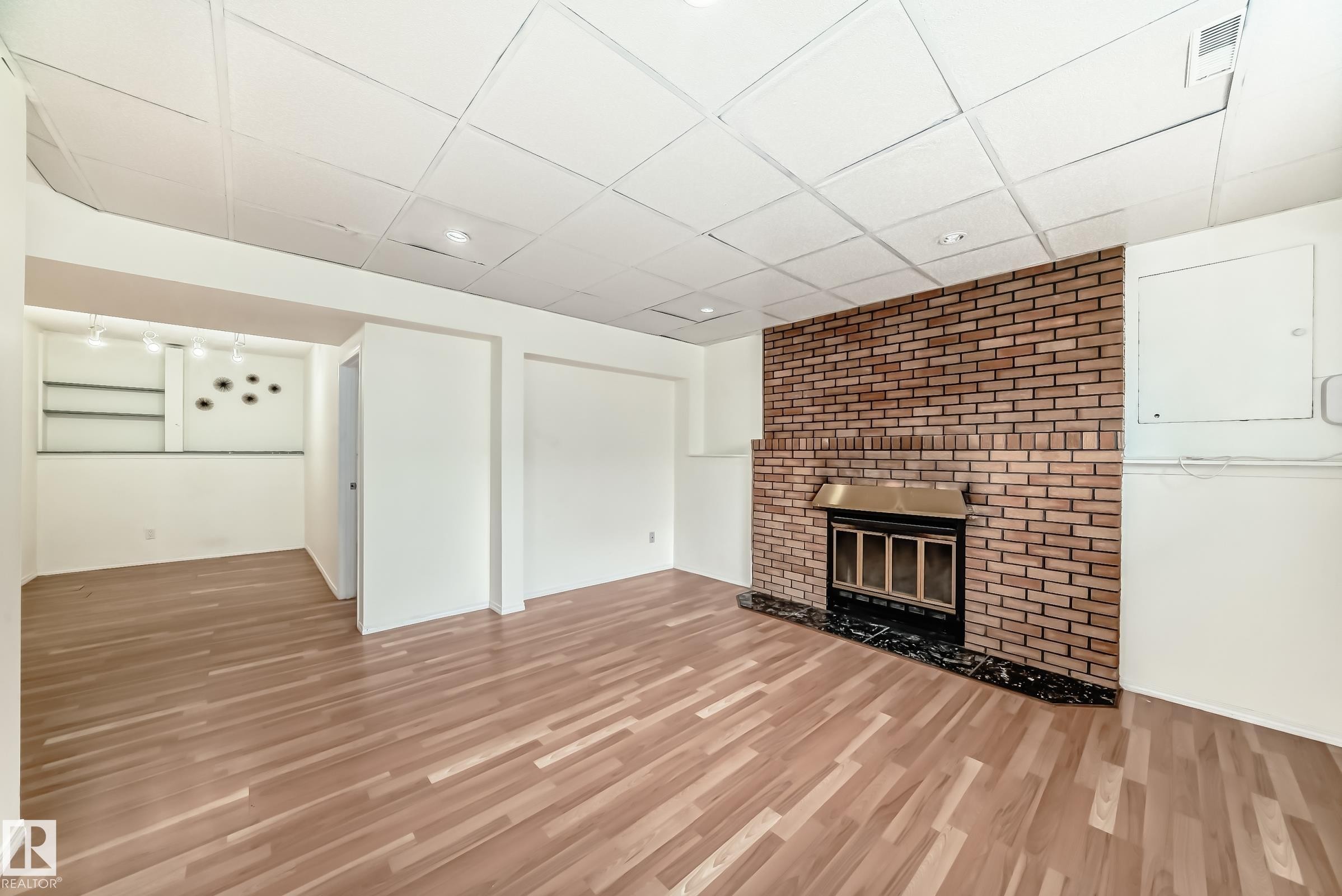 Spacious living area featuring wood-finish flooring, a brick-faced fireplace with a black marble hearth, and a dropped ceiling with recessed lighting - 2039 48 Street, Edmonton, AB - Indoor With Fireplace