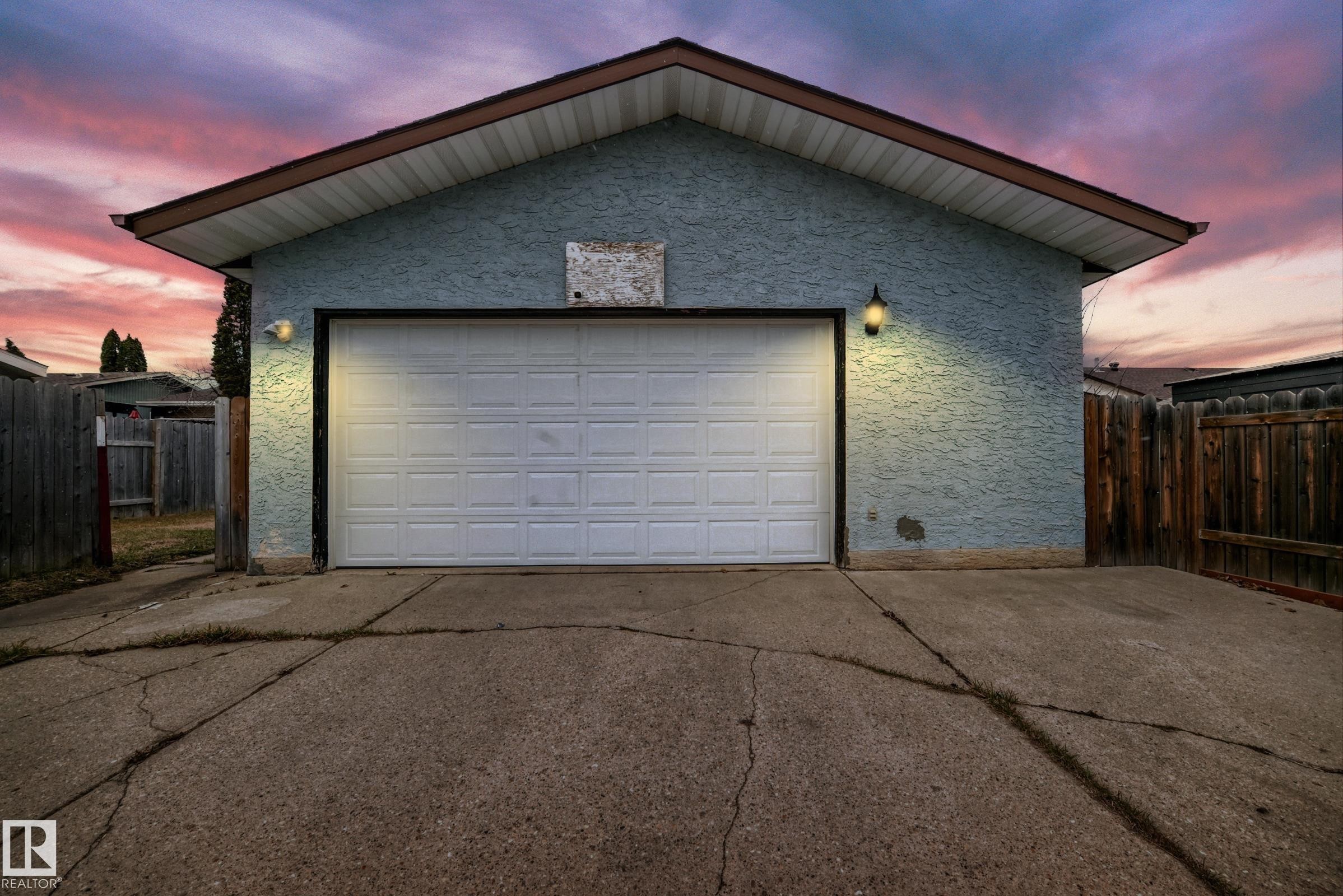 Detached garage featuring a white panel door, textured exterior siding, and two wall-mounted light fixtures - 2039 48 Street, Edmonton, AB - Outdoor With Exterior