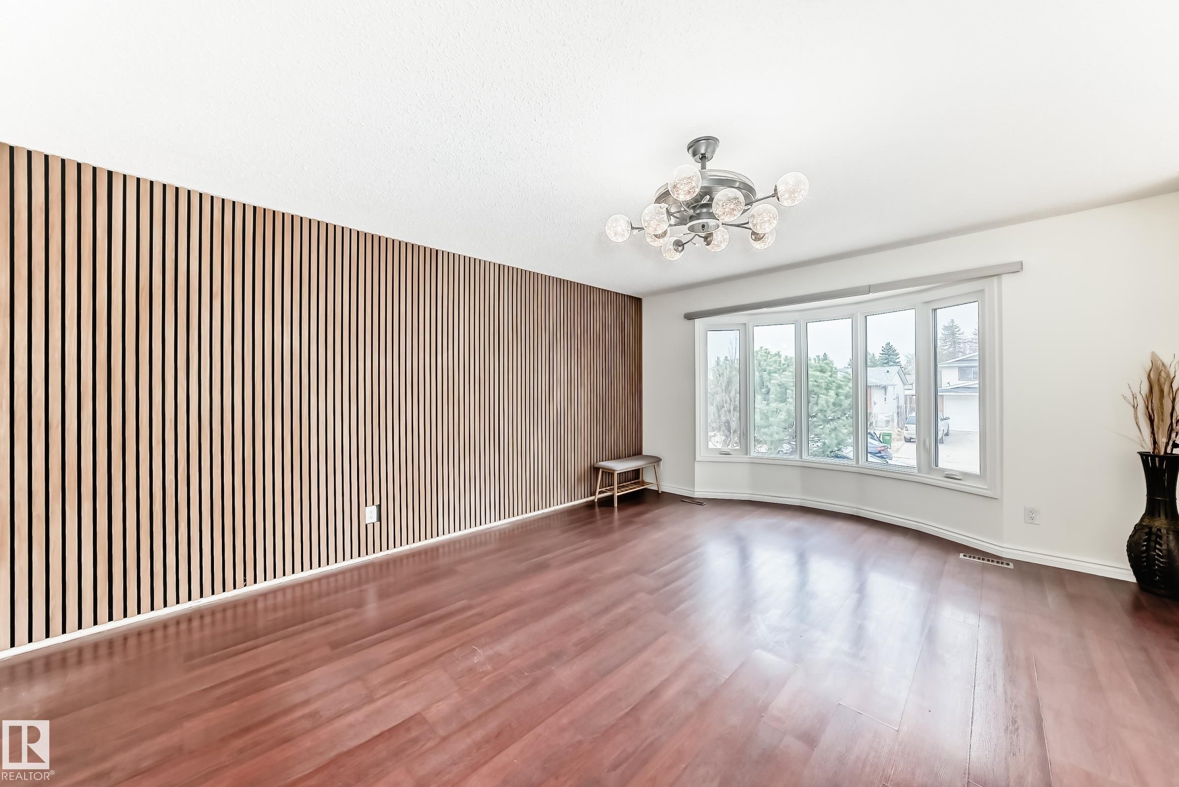 Spacious interior featuring a wood-slat accent wall, a wide bay window, and rich wood-finish flooring - 2039 48 Street, Edmonton, AB - Indoor Photo Showing Other Room