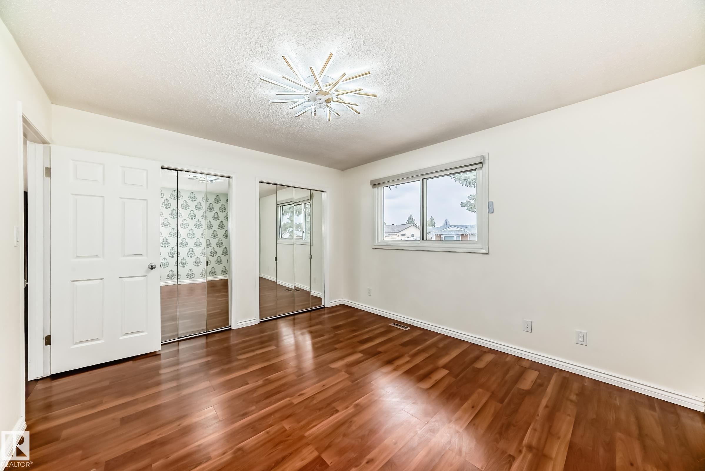 Room featuring wood-finish flooring, two sets of mirrored closet doors, a contemporary ceiling light fixture, and a window with a roller shade - 2039 48 Street, Edmonton, AB - Indoor Photo Showing Other Room