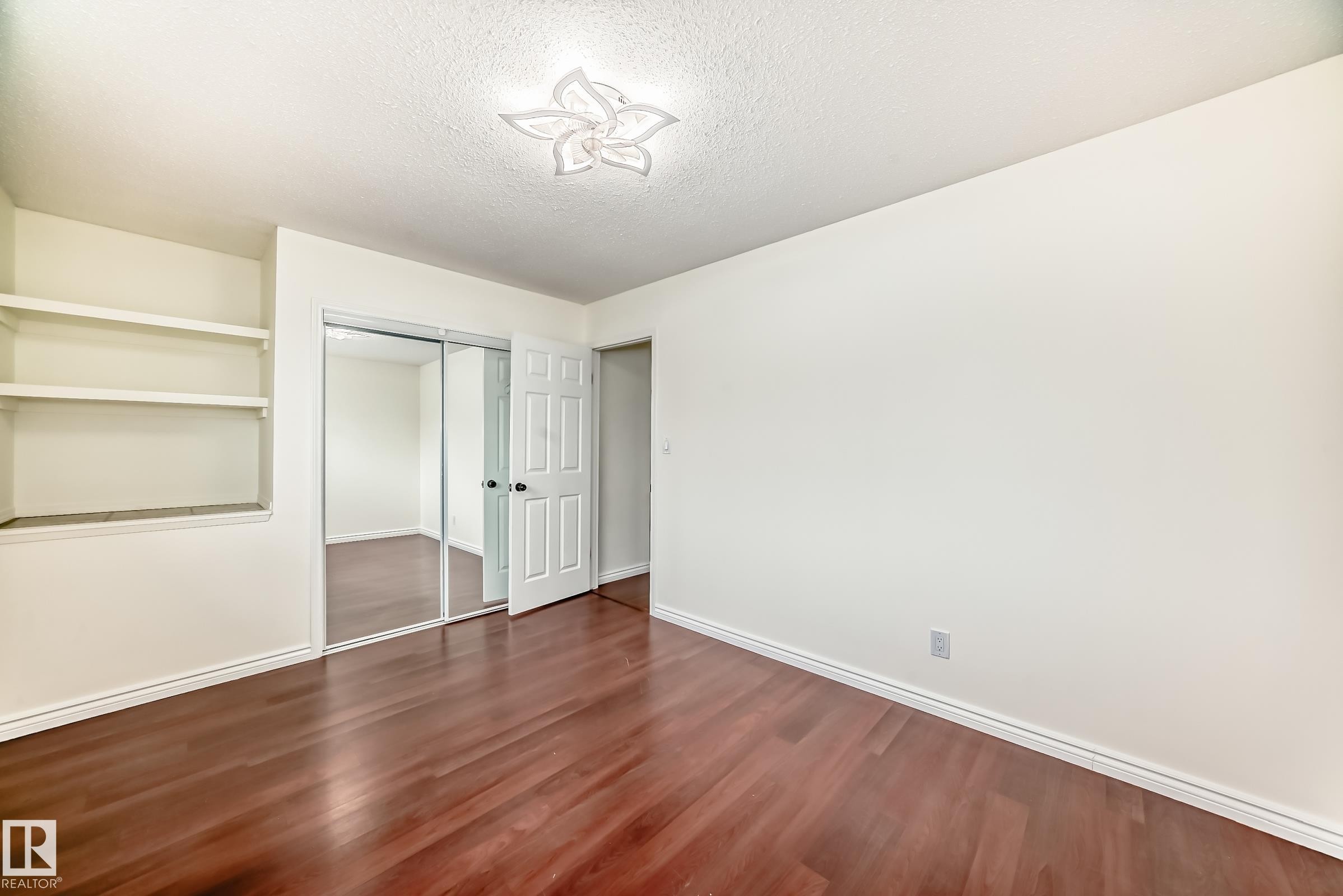 Room featuring wood-finish flooring, built-in shelving, mirrored closet doors, a paneled interior door, and a decorative ceiling light fixture - 2039 48 Street, Edmonton, AB - Indoor Photo Showing Other Room