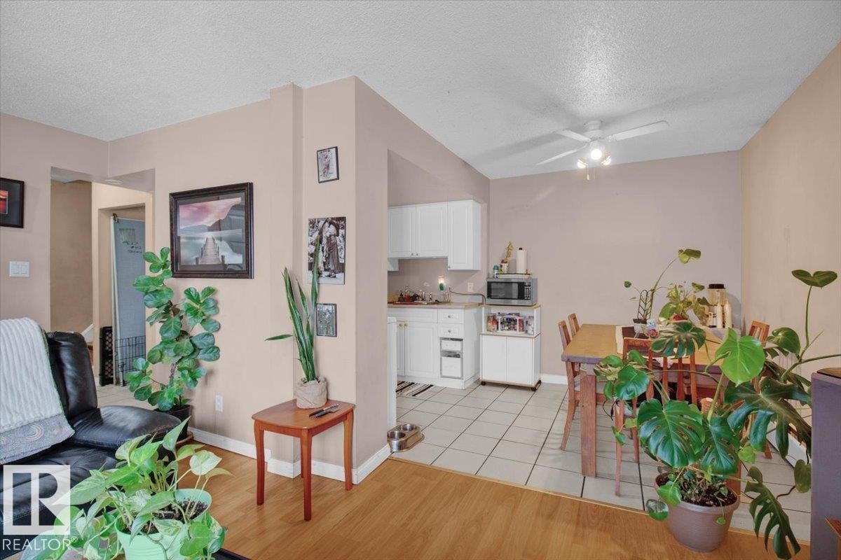 The property features an open-concept living area with hardwood flooring, leading to a kitchen with white cabinetry and tile flooring - 412 2908 116A Avenue, Edmonton, AB - Indoor