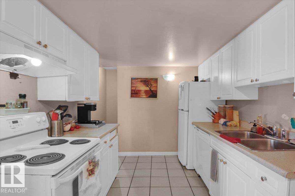 The kitchen features white cabinetry, light-colored countertops, a double basin sink, and tile flooring - 412 2908 116A Avenue, Edmonton, AB - Indoor Photo Showing Kitchen With Double Sink