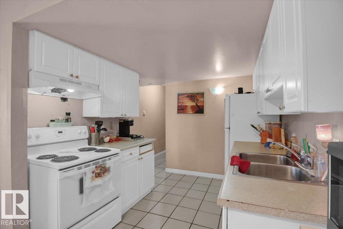 The kitchen features white cabinetry, a double basin sink, and a white oven with a range hood - 412 2908 116A Avenue, Edmonton, AB - Indoor Photo Showing Kitchen With Double Sink