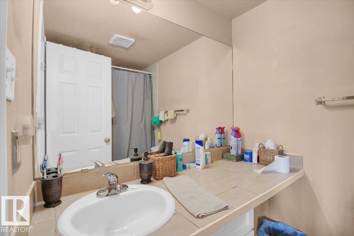 Bathroom featuring a vanity with an integrated sink, a tiled countertop, and a large wall-mounted mirror - 412 2908 116A Avenue, Edmonton, AB - Indoor Photo Showing Bathroom