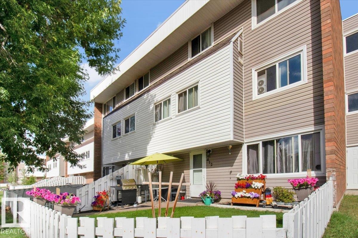The property features a multi-level exterior with siding, brick accents, and a white picket fence enclosing a lawn area - 412 2908 116A Avenue, Edmonton, AB - Outdoor