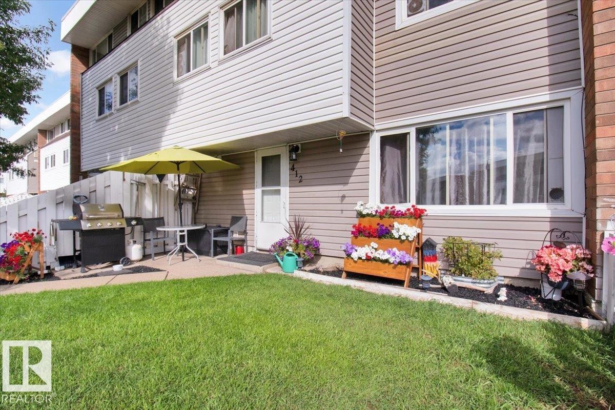 The property features a well-maintained lawn, a paved patio area, and a white picket fence - 412 2908 116A Avenue, Edmonton, AB - Outdoor With Deck Patio Veranda