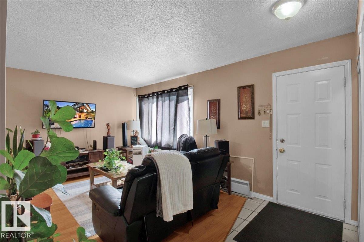 The living area features hardwood flooring, a white paneled entry door, and a window with dark curtains - 412 2908 116A Avenue, Edmonton, AB - Indoor