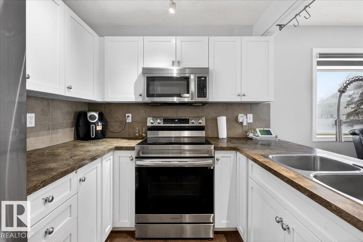 Kitchen with stainless steel appliances, white cabinets, and a textured ceiling - 47 230 Edwards Drive, Edmonton, AB - Indoor Photo Showing Kitchen With Double Sink