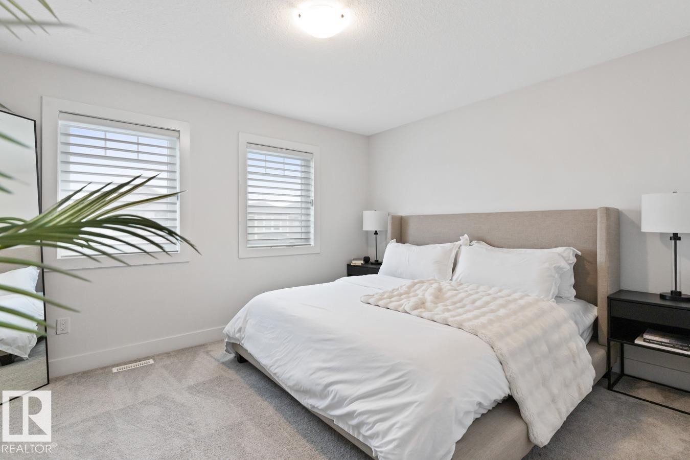 Carpeted bedroom featuring two windows with horizontal blinds, a neutral upholstered headboard, and a flush-mount ceiling light fixture - 6023 180 Avenue, Edmonton, AB - Indoor Photo Showing Bedroom