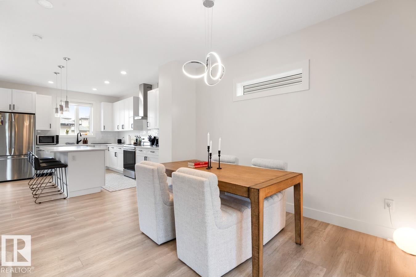Open-concept living space featuring wood-finish flooring, a contemporary dining light fixture, and a kitchen with white cabinetry, stainless steel appliances, and a central island with bar seating - 6023 180 Avenue, Edmonton, AB - Indoor Photo Showing Other Room