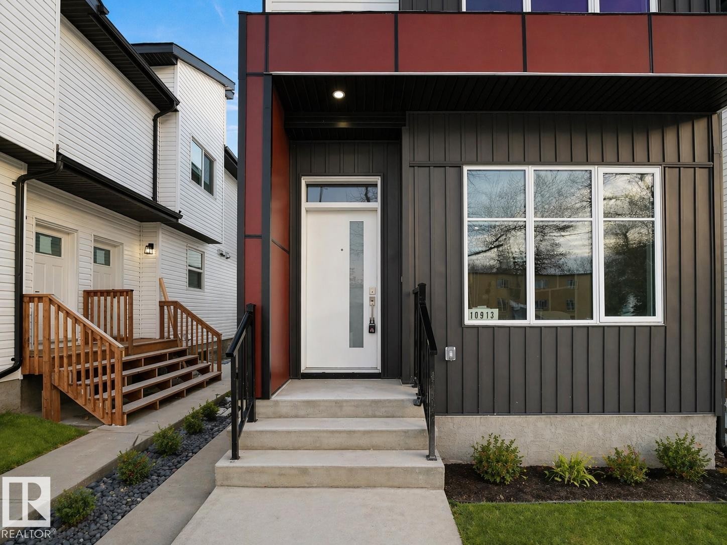 Modern exterior featuring a prominent white entry door with a vertical glass insert, concrete steps, and black metal handrails - 10913 159 Street, Edmonton, AB - Outdoor