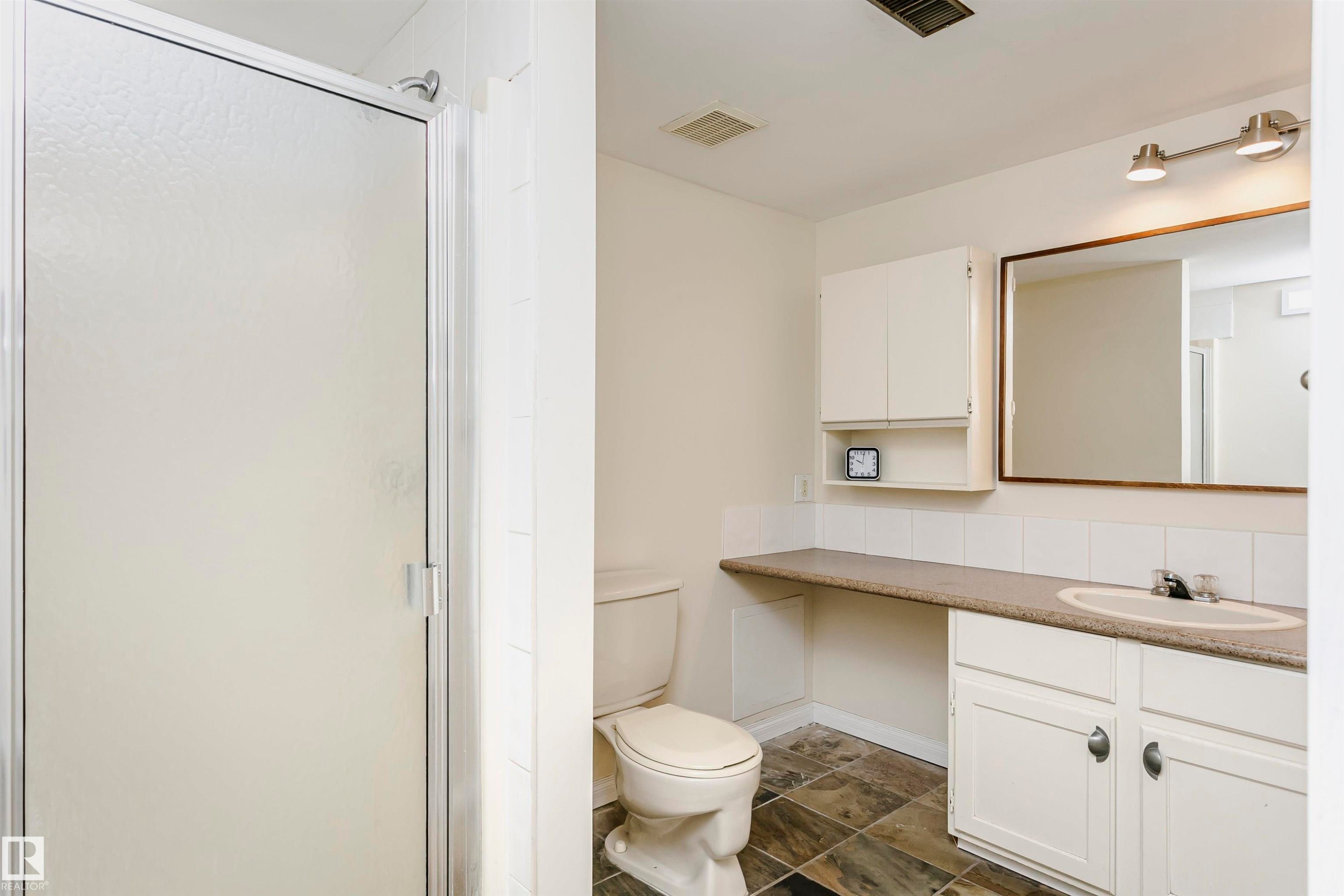 Bathroom featuring a frosted glass shower enclosure, a vanity with white cabinetry, an integrated sink, and a framed mirror - #303 10026 112 Street Nw, Edmonton, AB - Indoor Photo Showing Bathroom