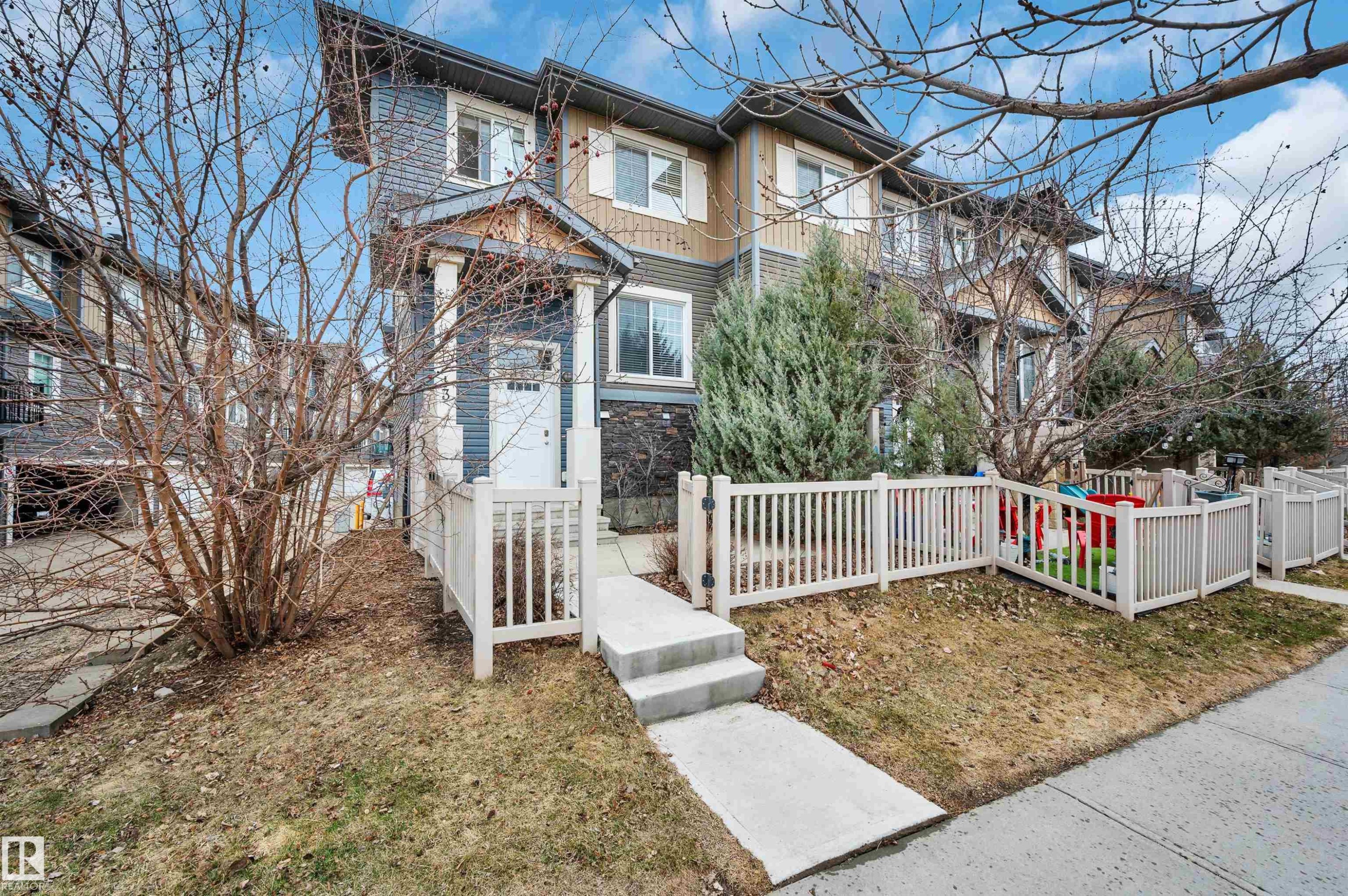 Multi-level townhouse exterior featuring a covered entry, white picket fencing, and a concrete walkway - 13 1030 Chappelle Boulevard, Edmonton, AB - Outdoor