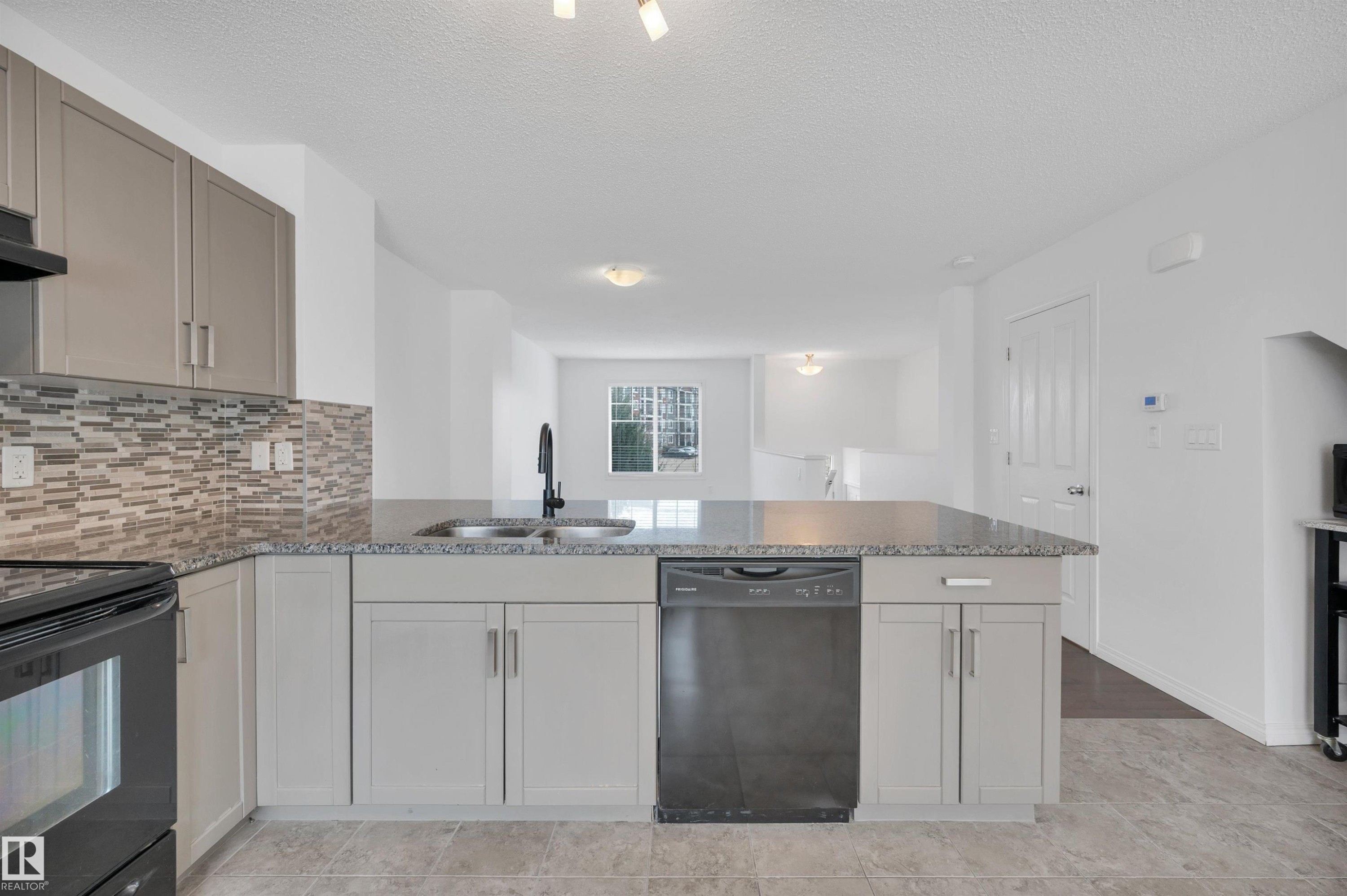 Kitchen with light gray cabinetry, a mosaic tile backsplash, and a dark stone-finish countertop - 13 1030 Chappelle Boulevard, Edmonton, AB - Indoor Photo Showing Kitchen With Double Sink