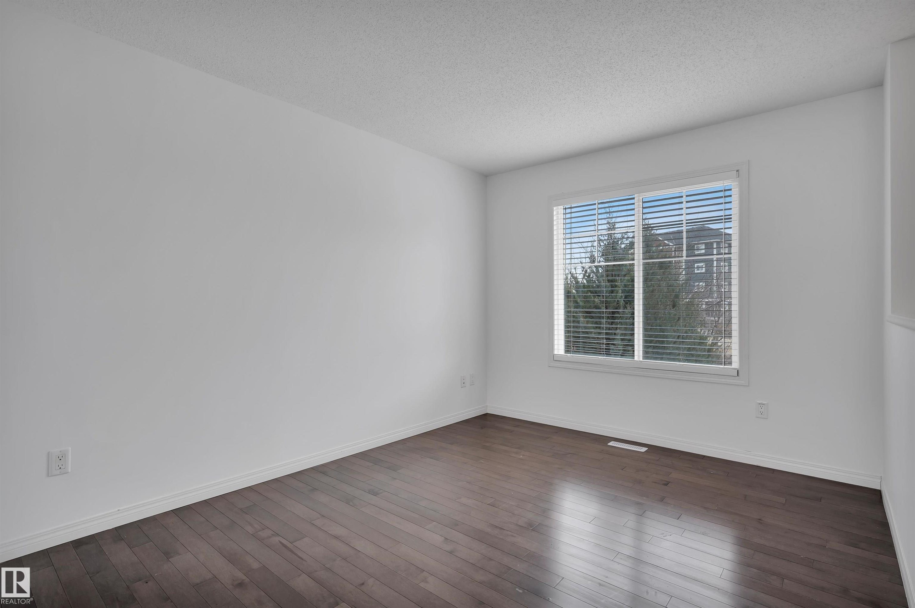 Spacious room featuring wood-finish flooring, white walls, and a large window with blinds - 13 1030 Chappelle Boulevard, Edmonton, AB - Indoor Photo Showing Other Room