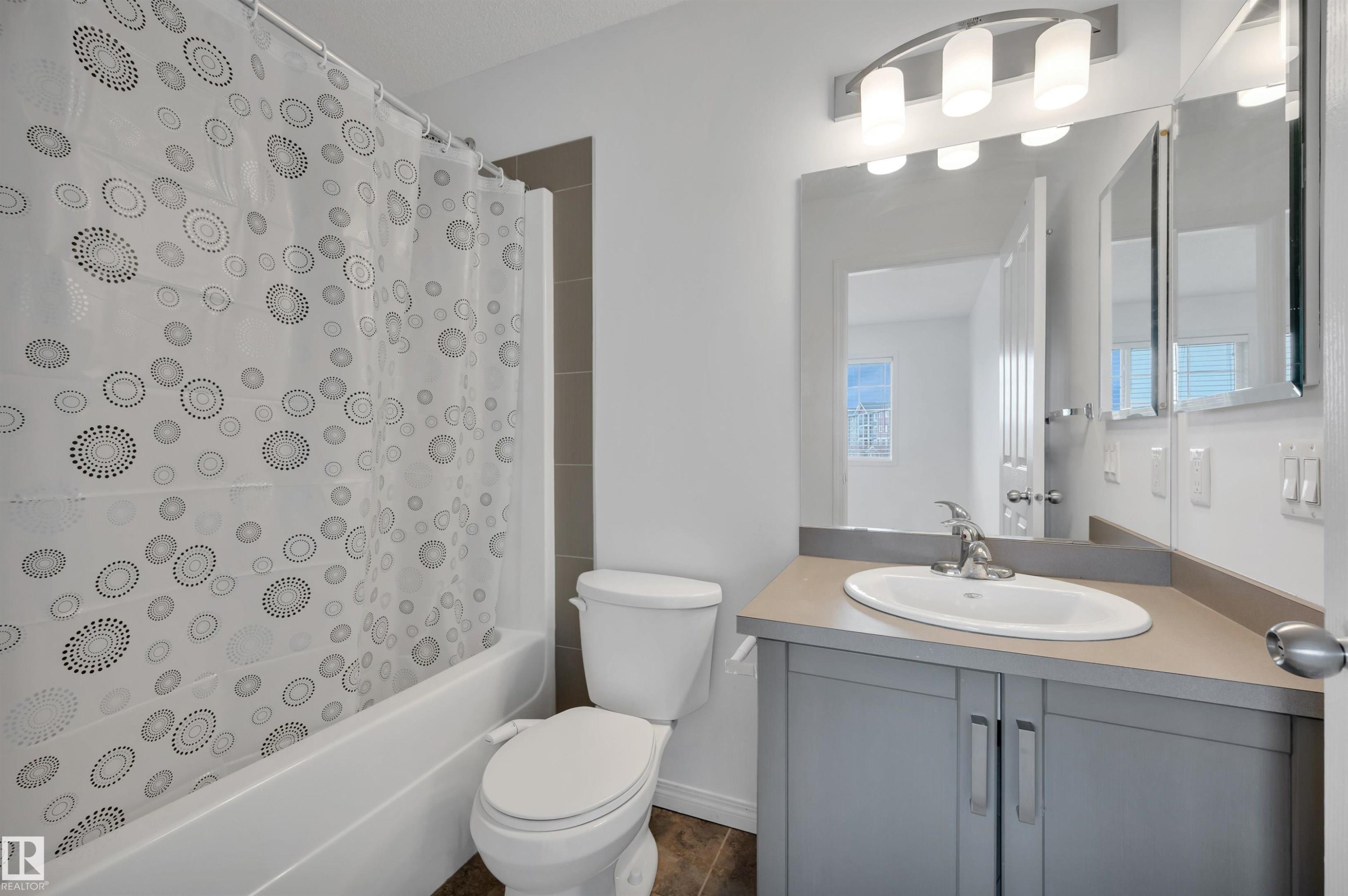 Bathroom featuring a white bathtub with tile surround, a toilet, and a vanity with an integrated sink - 13 1030 Chappelle Boulevard, Edmonton, AB - Indoor Photo Showing Bathroom